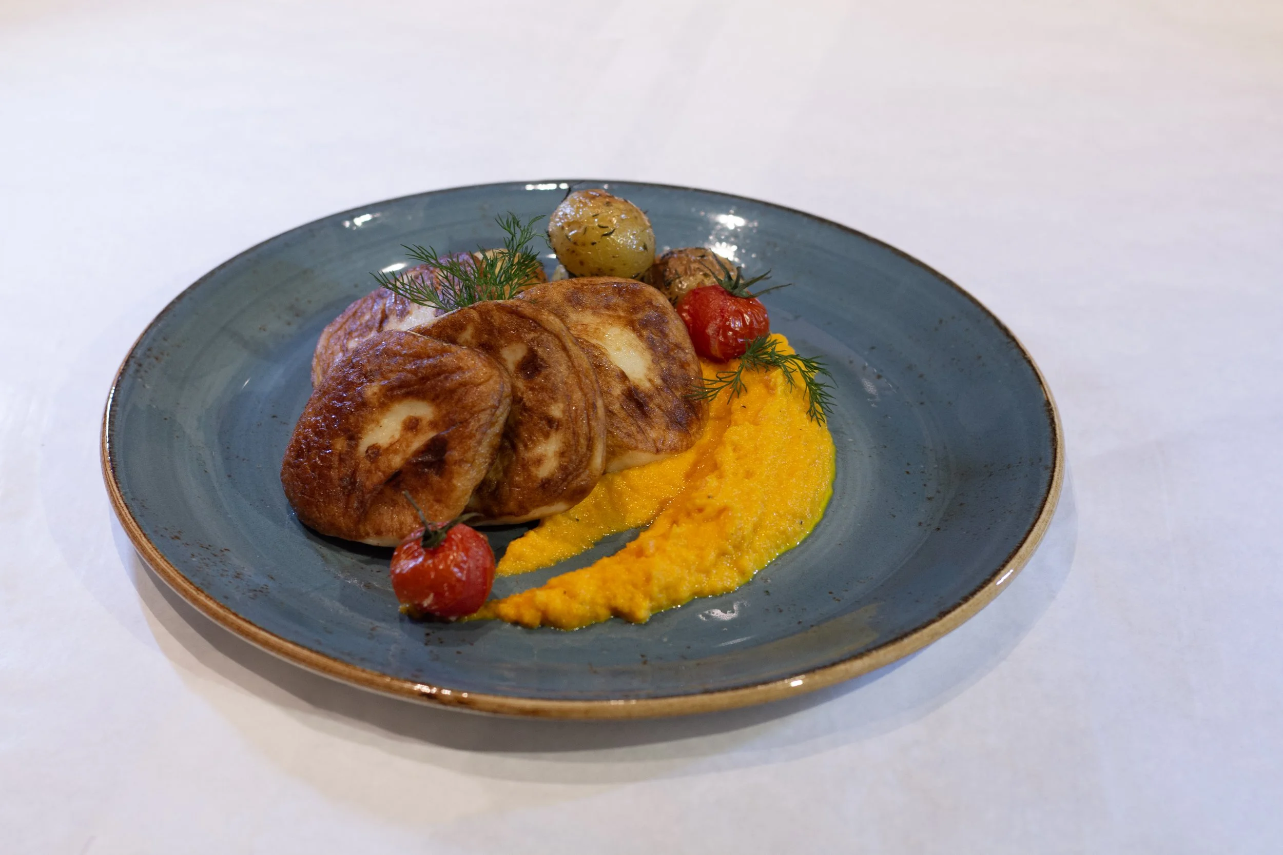 Plate of roasted chicken with vegetables including cherry tomatoes, potatoes, and herbs, served with mashed sweet potatoes.