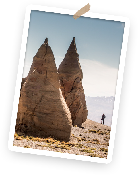 Two large rock formations in a desert with a person standing in the distance and a clear sky overhead.