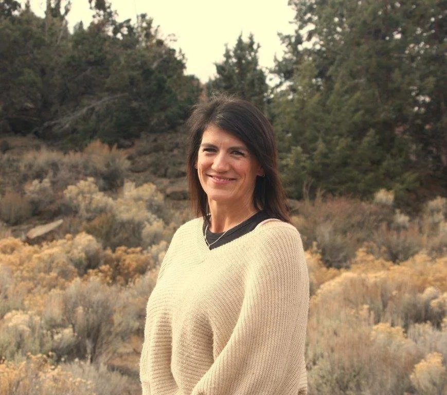 Smiling person with long dark hair standing in front of leafy background