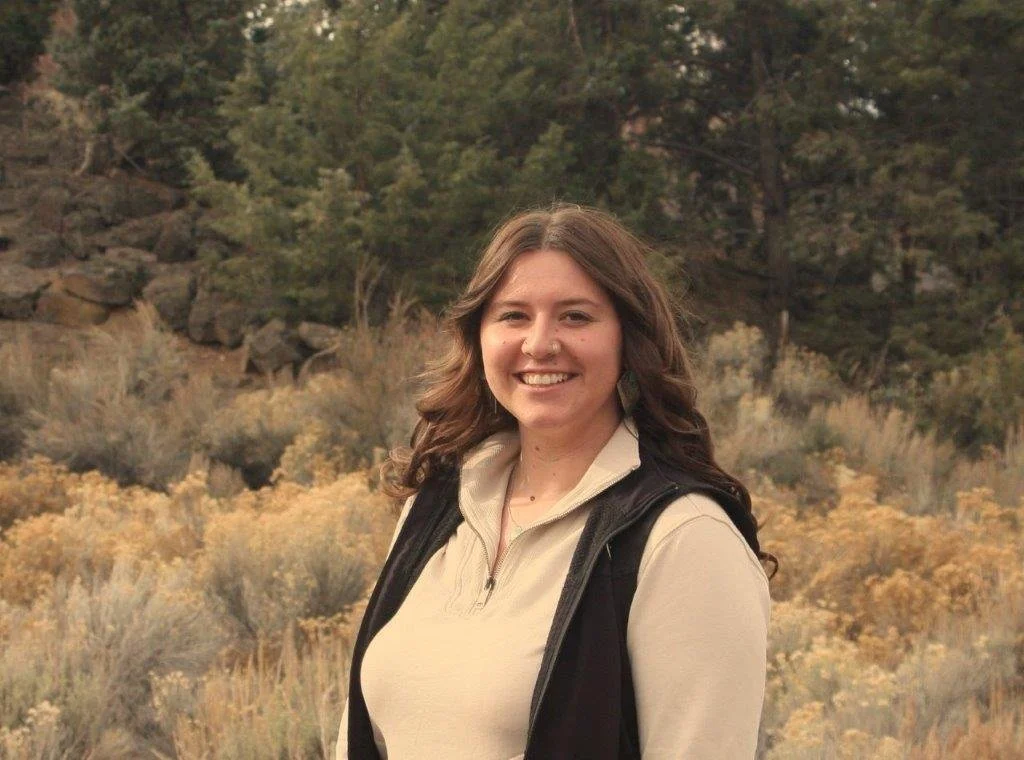 Smiling person with long hair, wearing a turquoise necklace, close-up portrait.