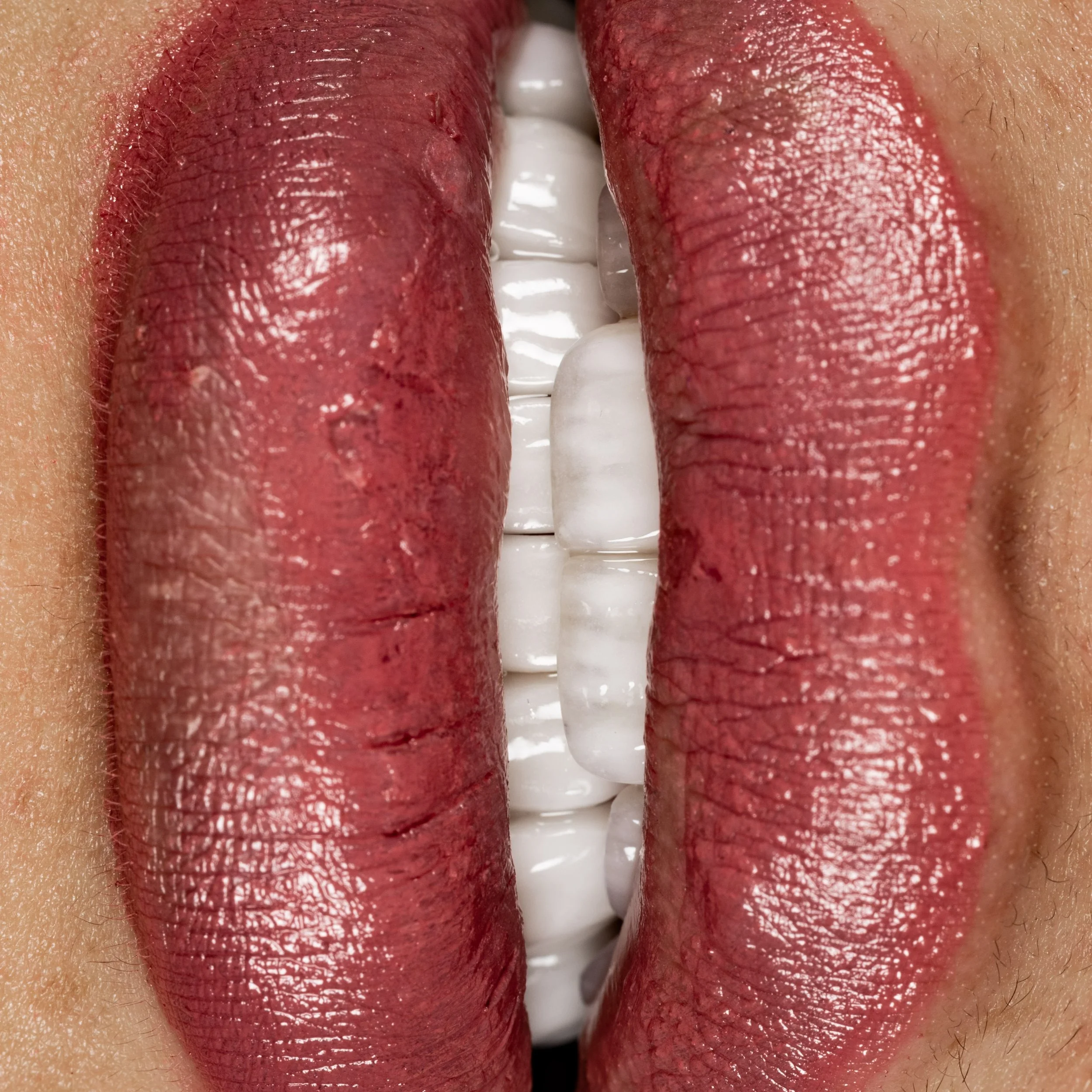 Close-up of lips with red lipstick and teeth visible between them.