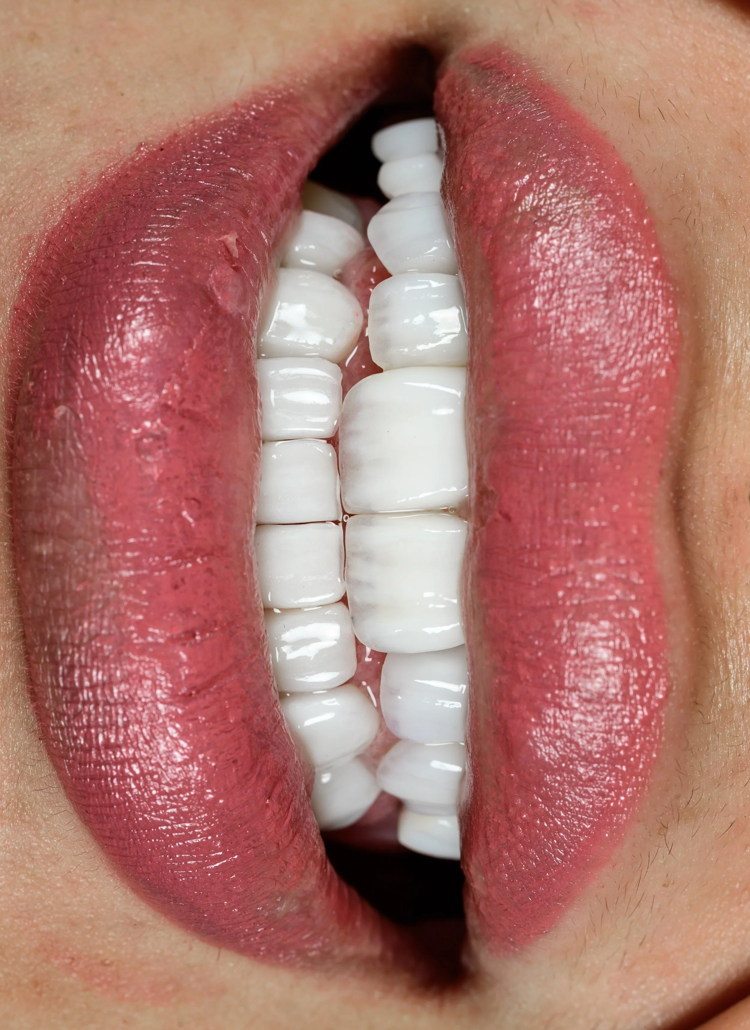 Close-up of lips with pink lipstick slightly parted, revealing white teeth.