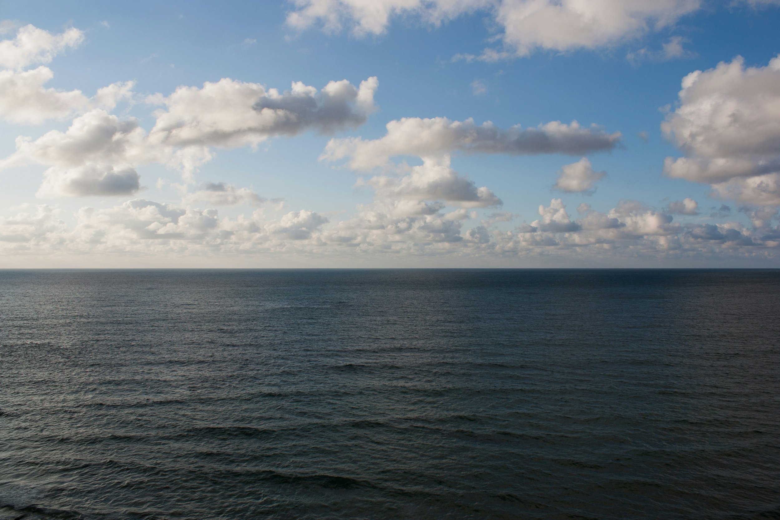 A vast ocean with small waves under a partly cloudy sky with white and gray clouds.