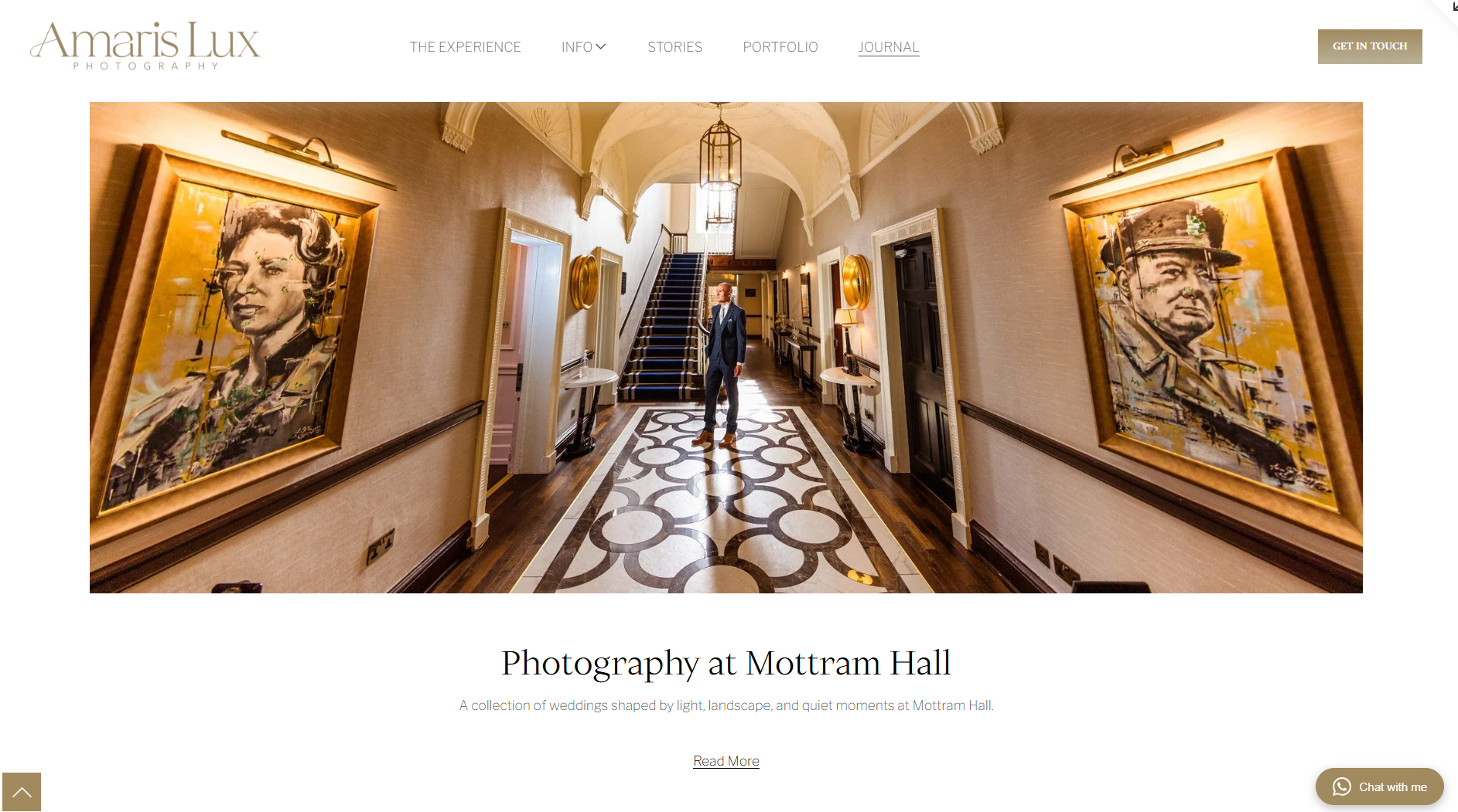 Interior hallway of a building with artwork on the walls, a man in a suit standing in the center, and a staircase at the end.