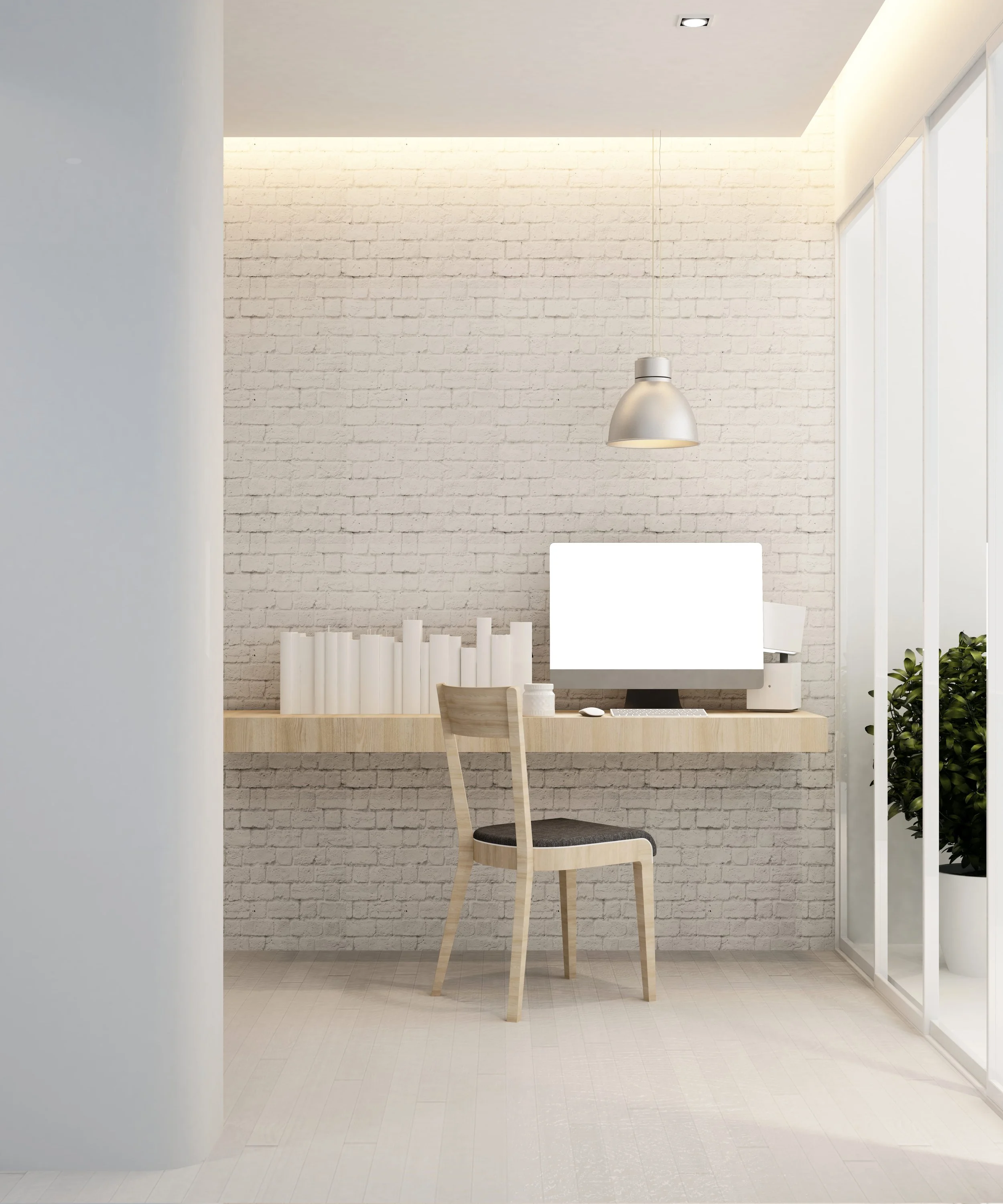 Minimalist home office with a white brick wall, a wooden desk with a computer, a single chair, a hanging pendant light, and a large window with potted plants.