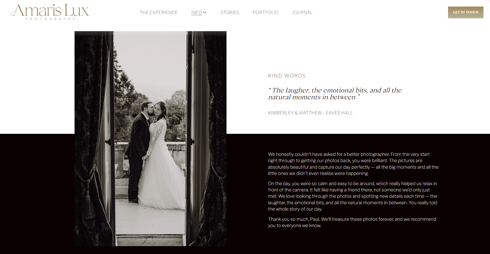 Black and white photograph of a bride and groom standing outside on a balcony, framed by two open dark curtains, holding hands and looking at each other, with a scenic outdoor background.