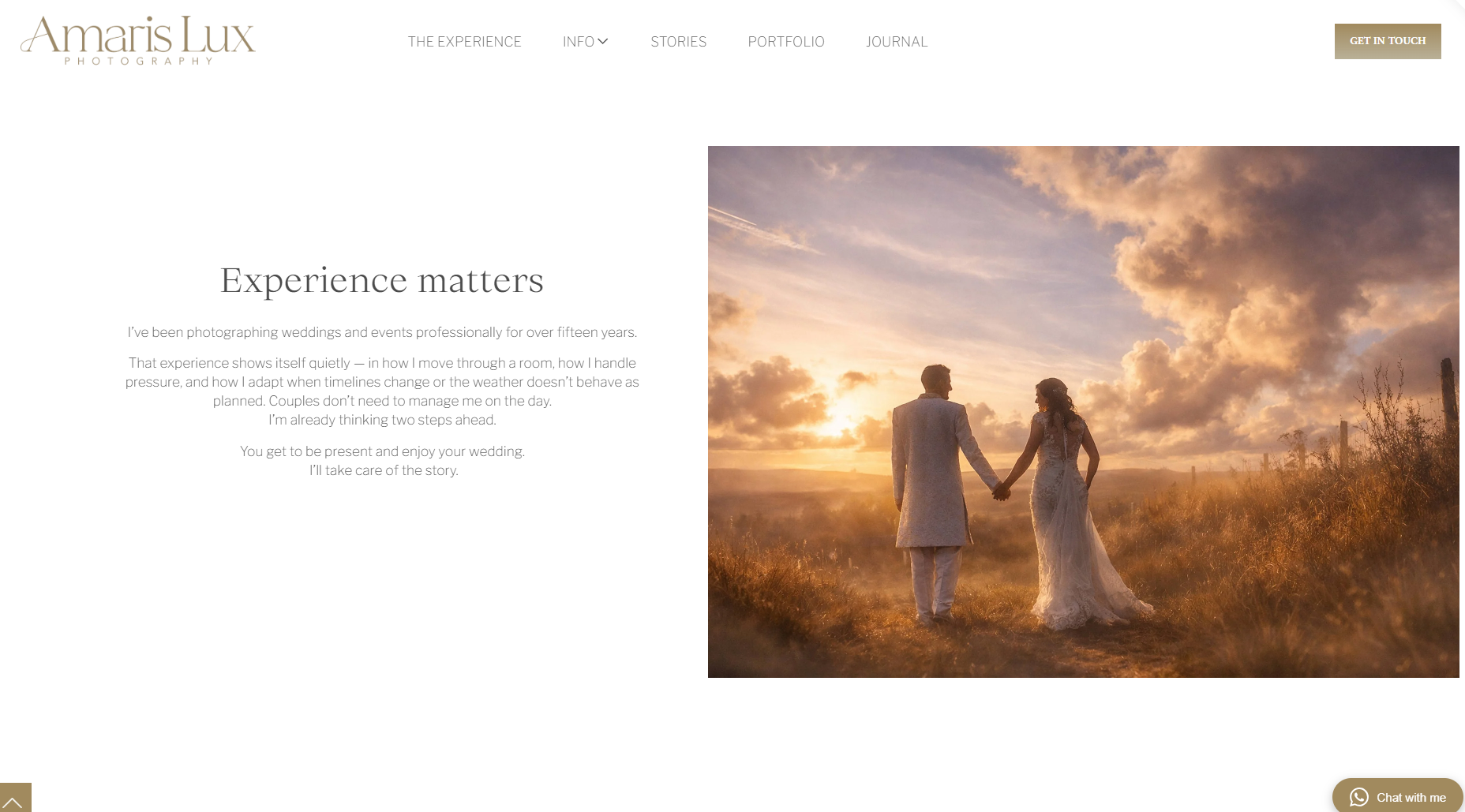A couple in wedding attire holding hands, walking in a field at sunset with dramatic clouds in the sky.