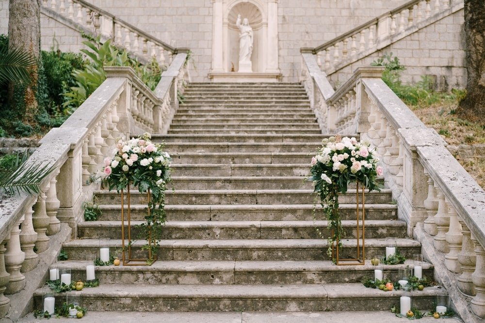 Decorative stone staircase with flower arrangements, candles, and apples, leading up to a historic sculpture in an outdoor setting.