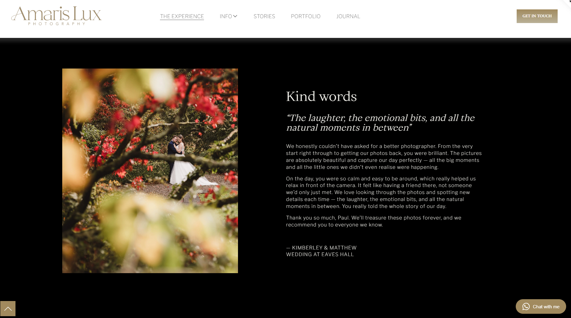 A wedding photo of a bride and groom standing in a garden surrounded by red flowers and greenery, partially obscured by tree branches.