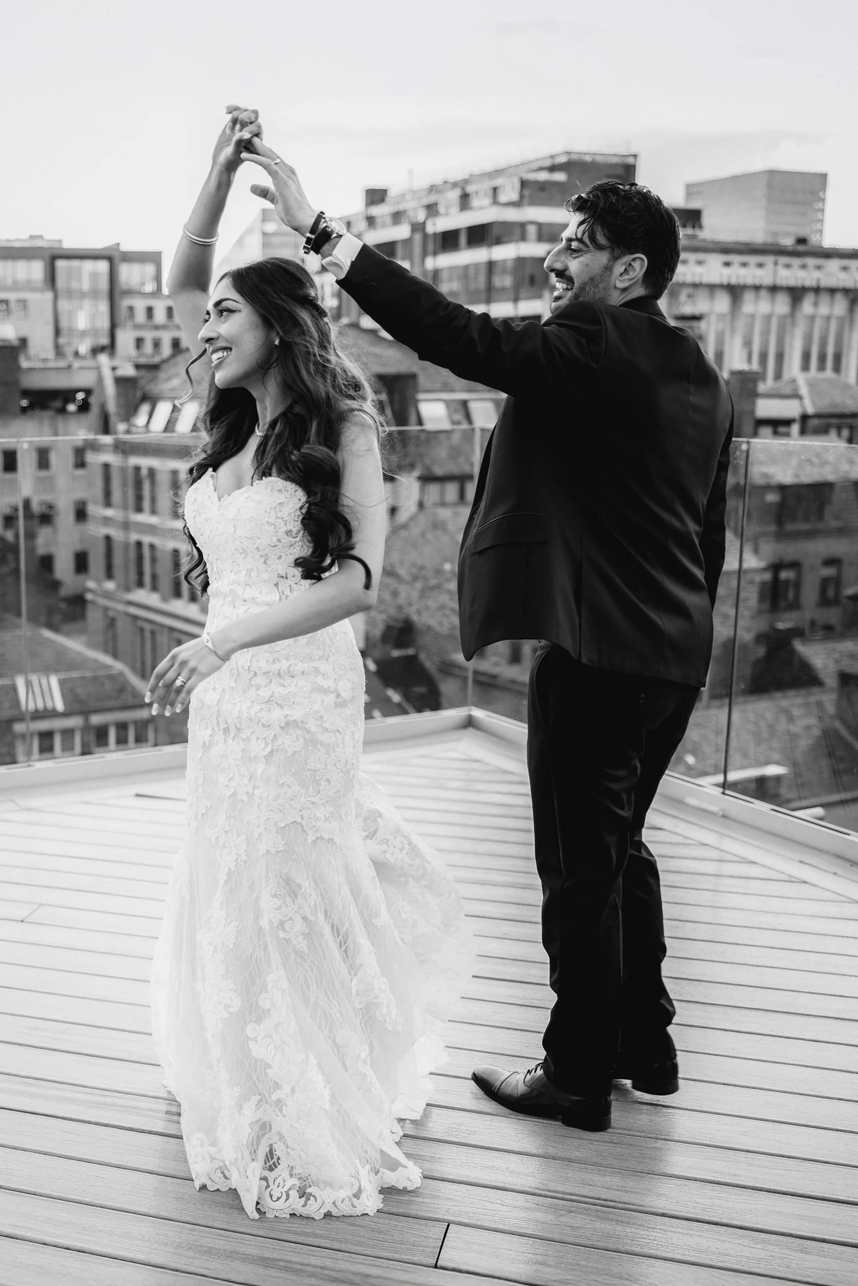 A couple dancing on a rooftop with city buildings in the background, black and white photo.