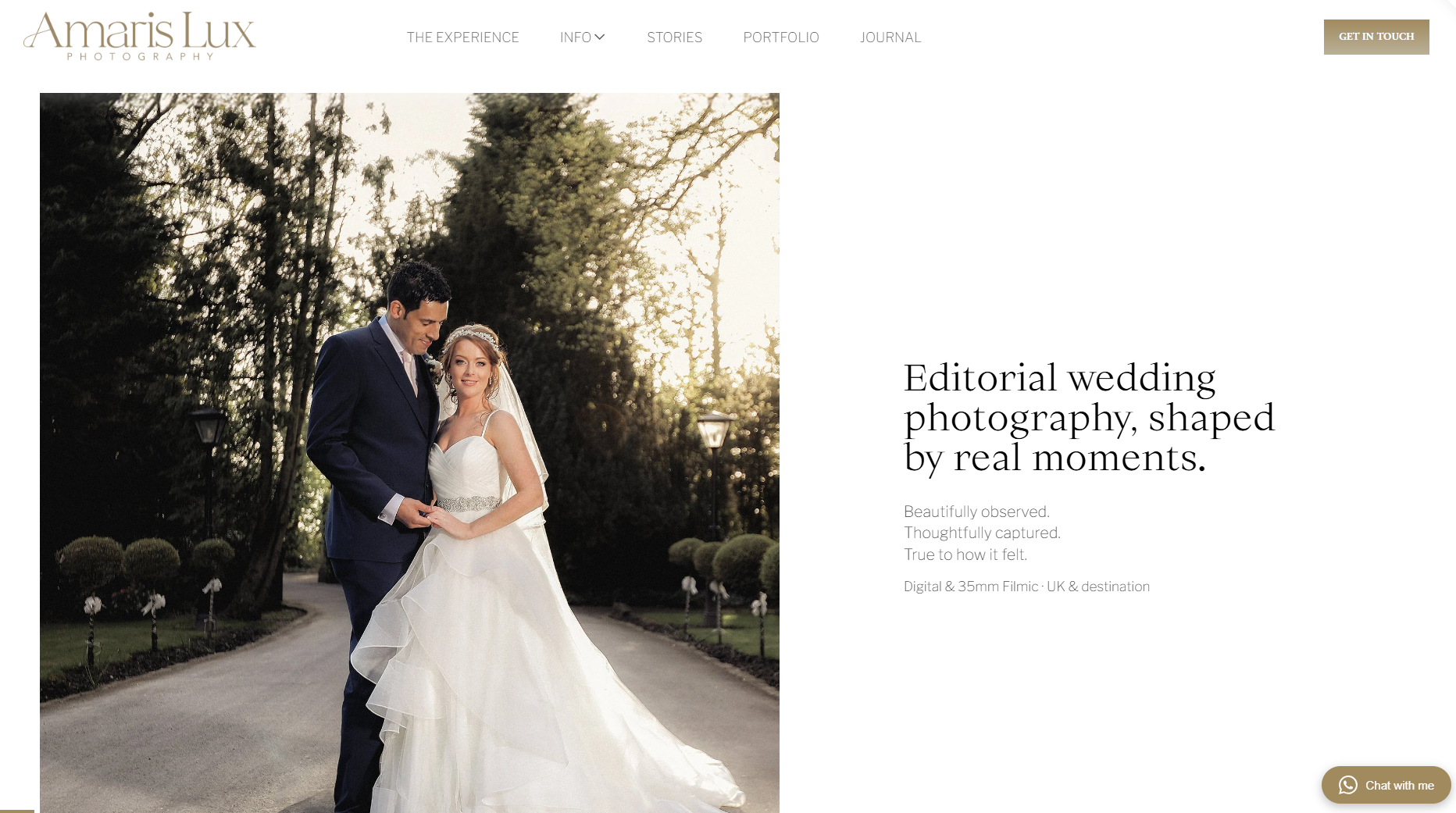 A bride and groom standing outdoors on a pathway surrounded by trees and bushes, with the bride in a white wedding gown and veil, and the groom in a dark suit, during sunset.