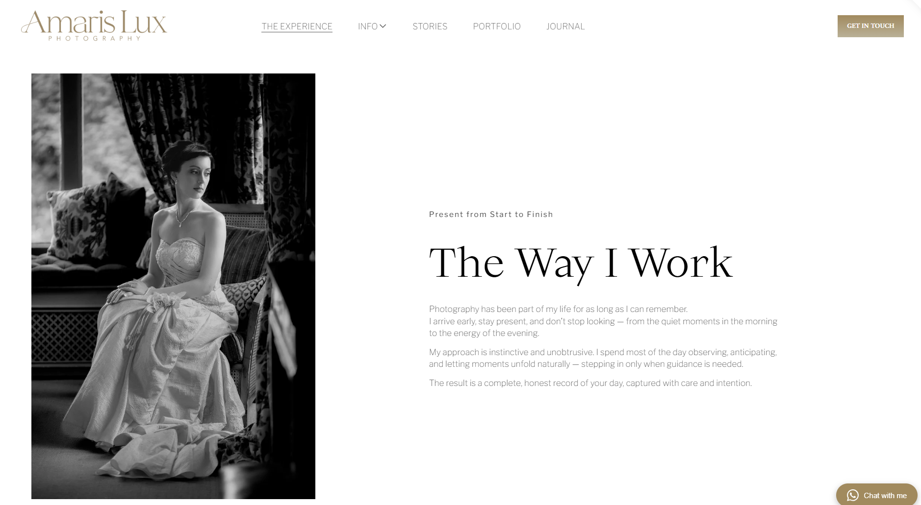 A woman in a wedding dress sitting on a chair indoors, with dark patterned curtains and a window behind her, captured in black and white.