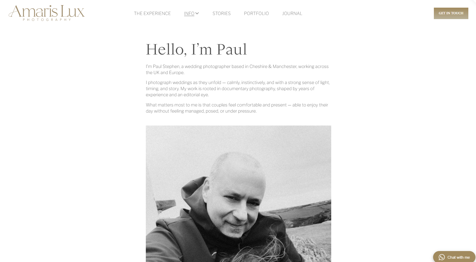 A black and white portrait photograph of a man outdoors, with a landscape of fields and distant hills in the background.