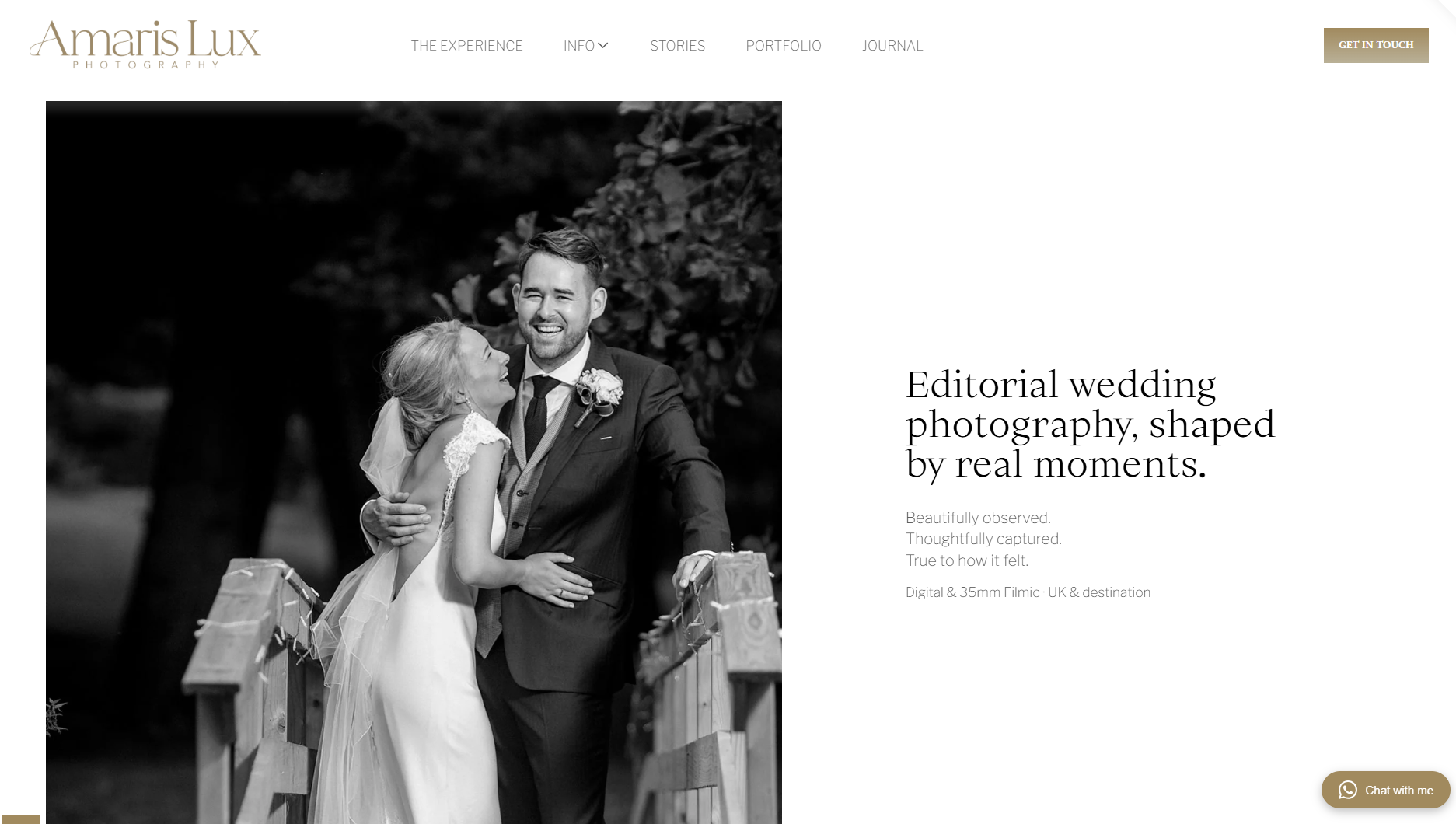 Black and white photograph of a bride and groom sharing a joyful moment outdoors, with the bride smiling and the groom squinting as they embrace near a wooden fence, surrounded by trees.