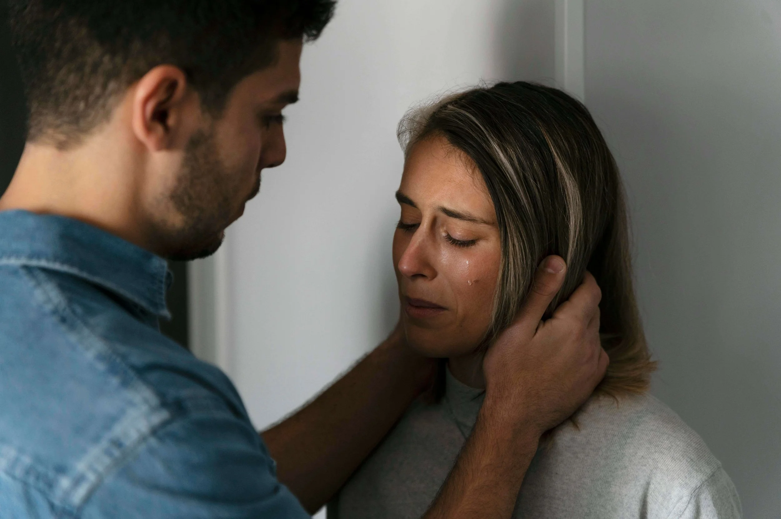 Man placing his hands on a woman's face as she cries. Reclaim your freedom and rebuild a safety and self-worth with the help of therapy for intimate partner violence in New York, NY.