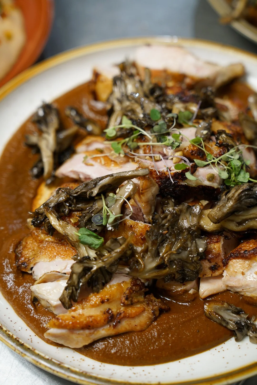 Plate of roasted chicken topped with sautéed mushrooms and microgreens, served with brown sauce.