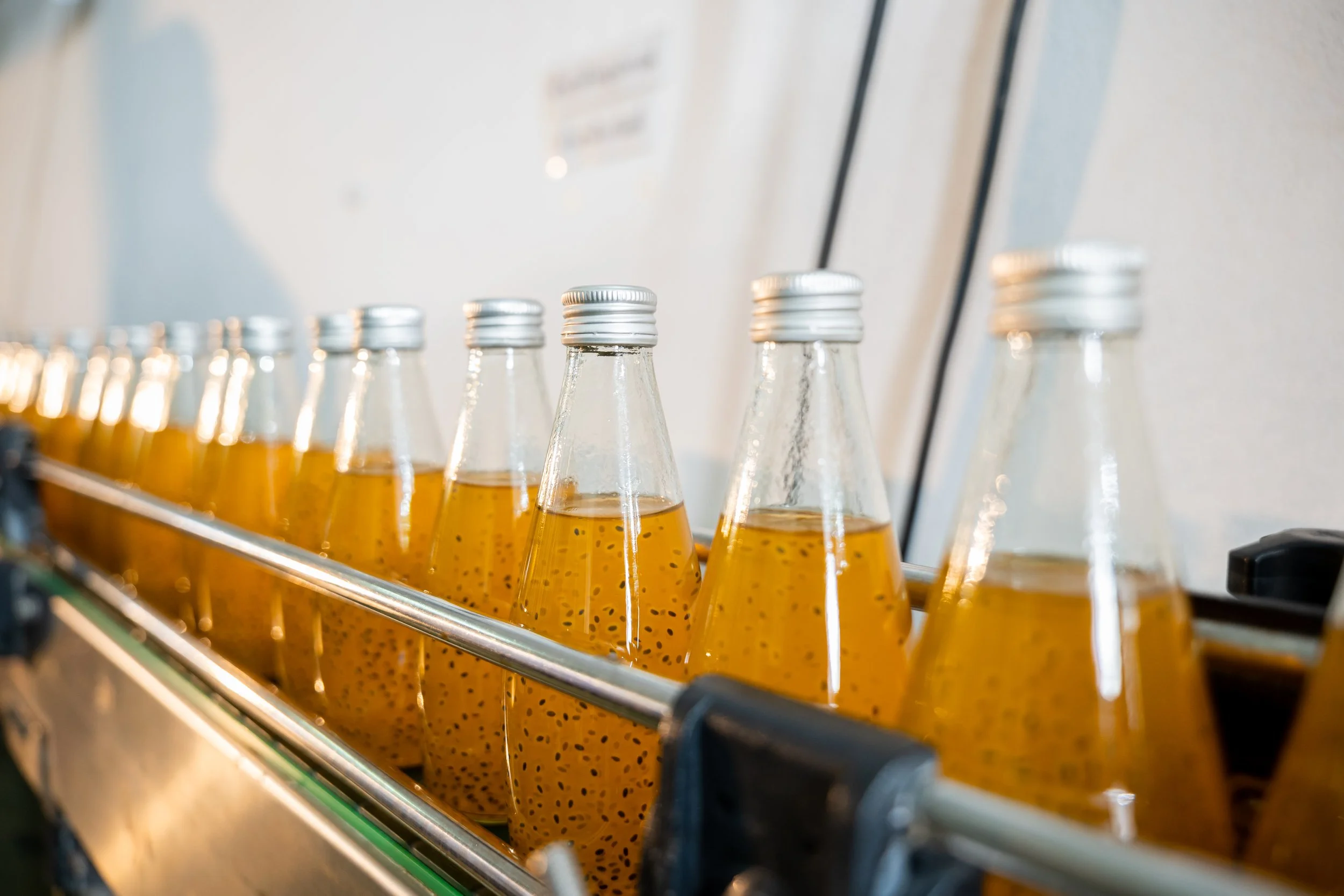 Bottles of orange-colored liquid with seeds on a conveyor belt.