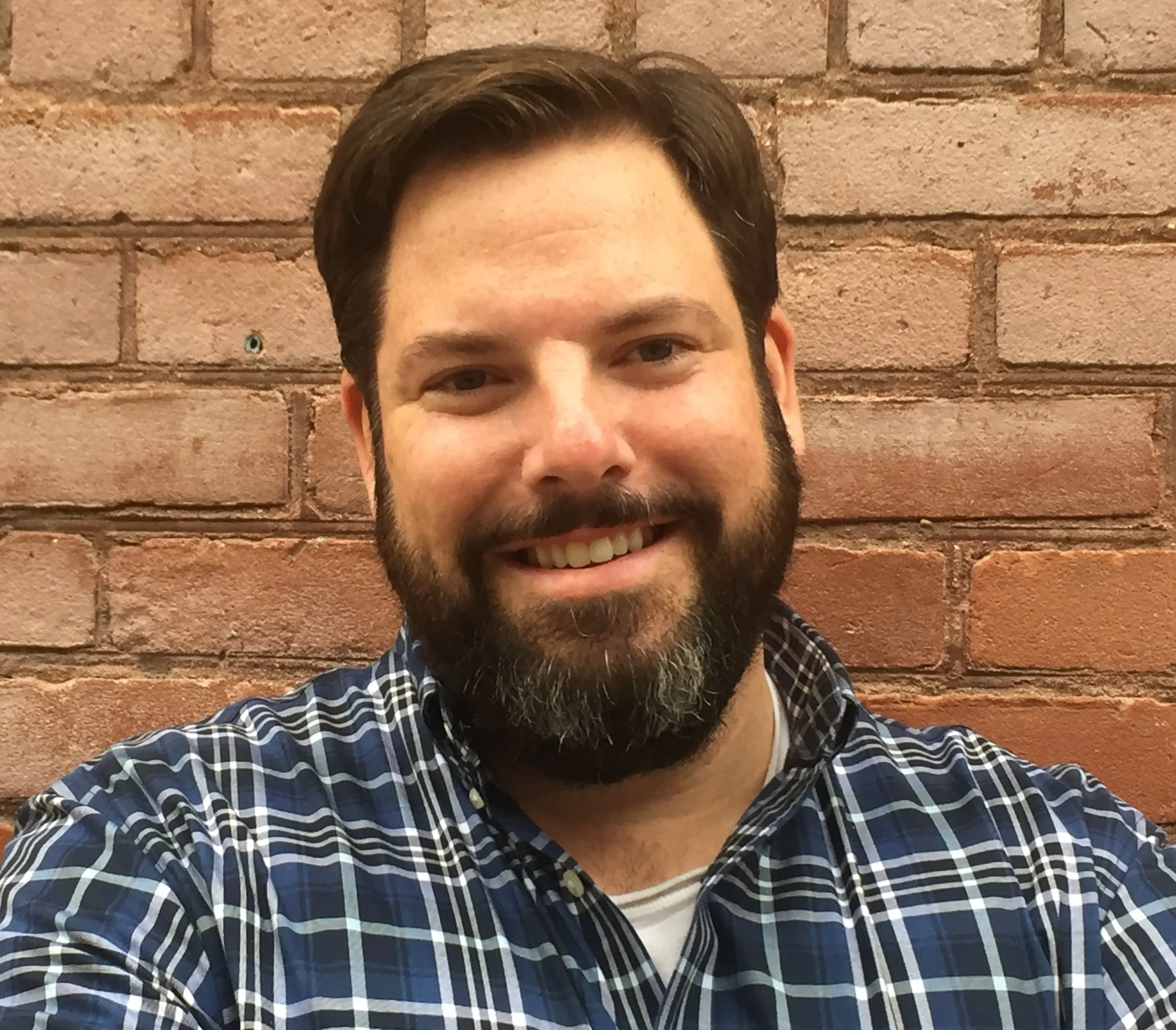 Attorney John McCarthy in front of a brick building wearing a blue plaid shirt.