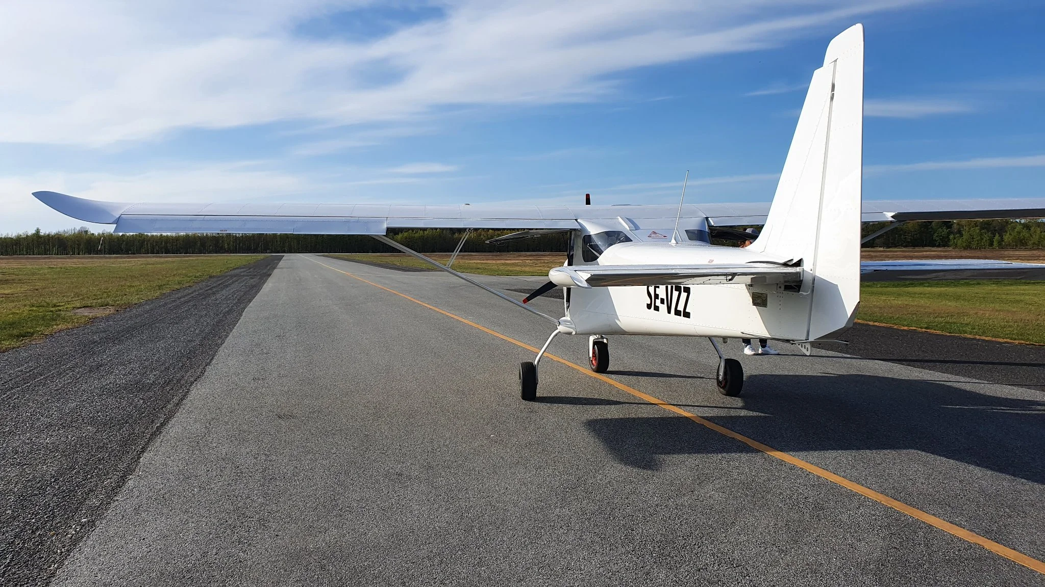 Litet flygplan på en landningsbana med blå himmel och skog i bakgrunden.