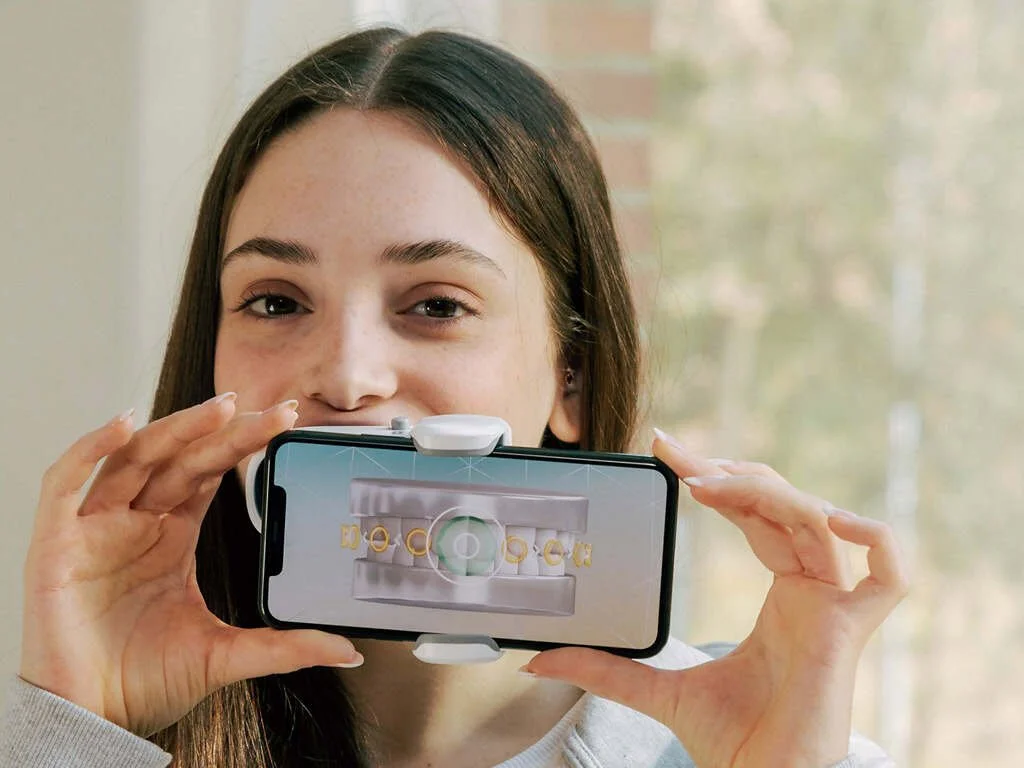 Young woman holding a smartphone with an image of dental braces displayed on the screen.
