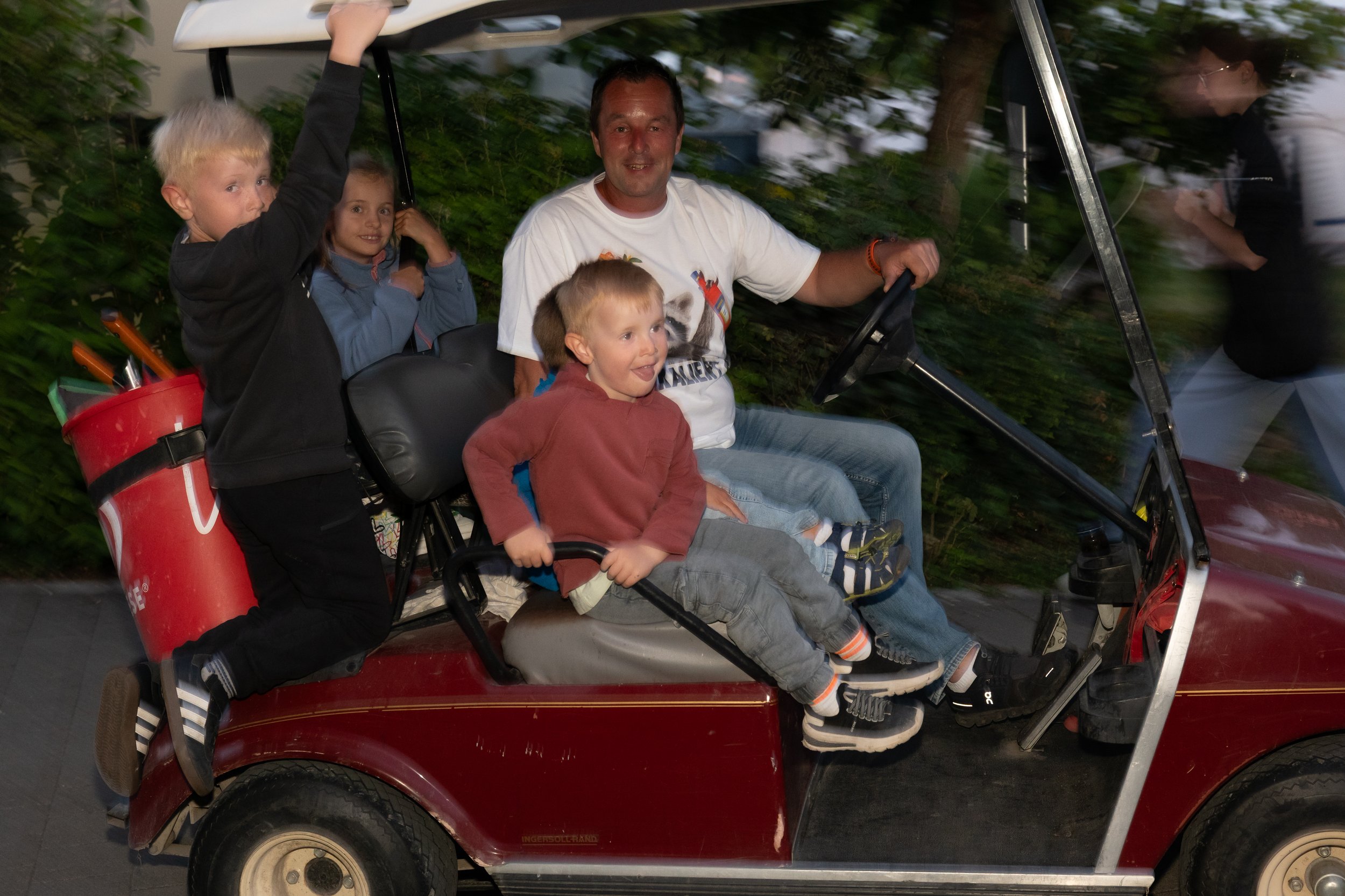 Eine Familie mit vier Kindern fährt in einem kleinen, roten Golfwagen.