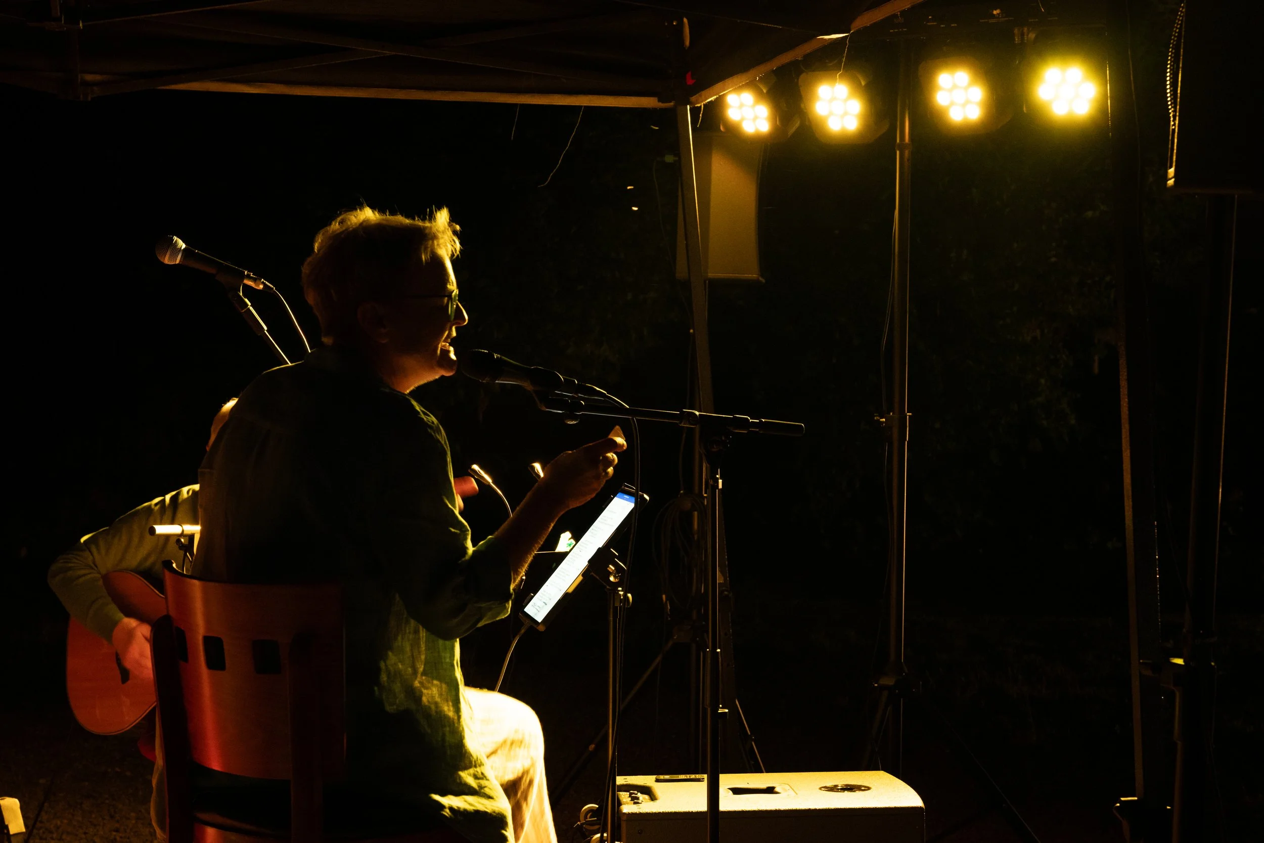 Ein Musiker beim Singen und Gitarrespielen bei einem nächtlichen Open-Air-Konzert, beleuchtet von Bühnenlicht.