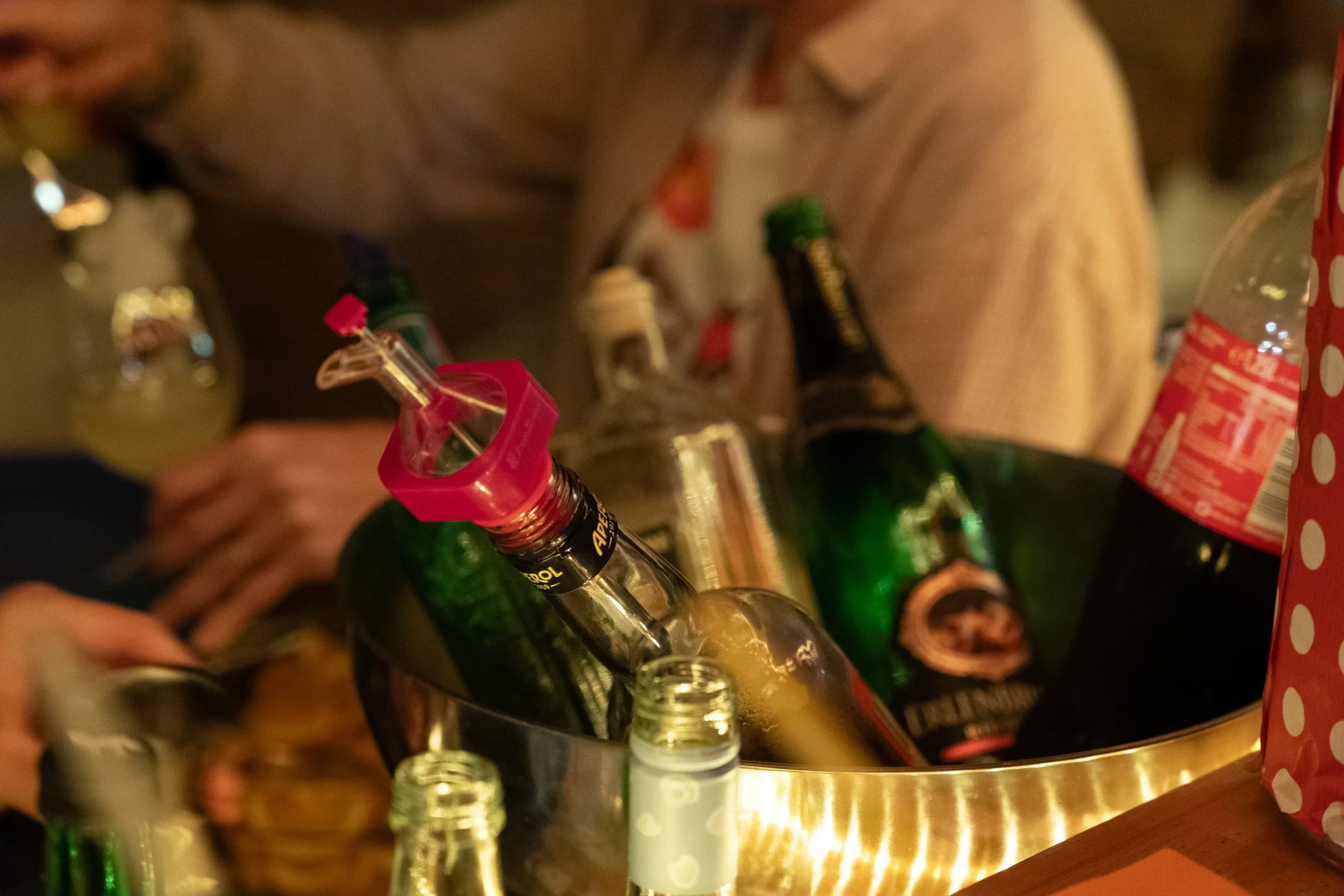 Bierflaschen in einem Eimer mit Eis, umgeben von weiteren Flaschen und Getränkeflaschen auf einem Tisch, bei einer geselligen Zusammenkunft.
