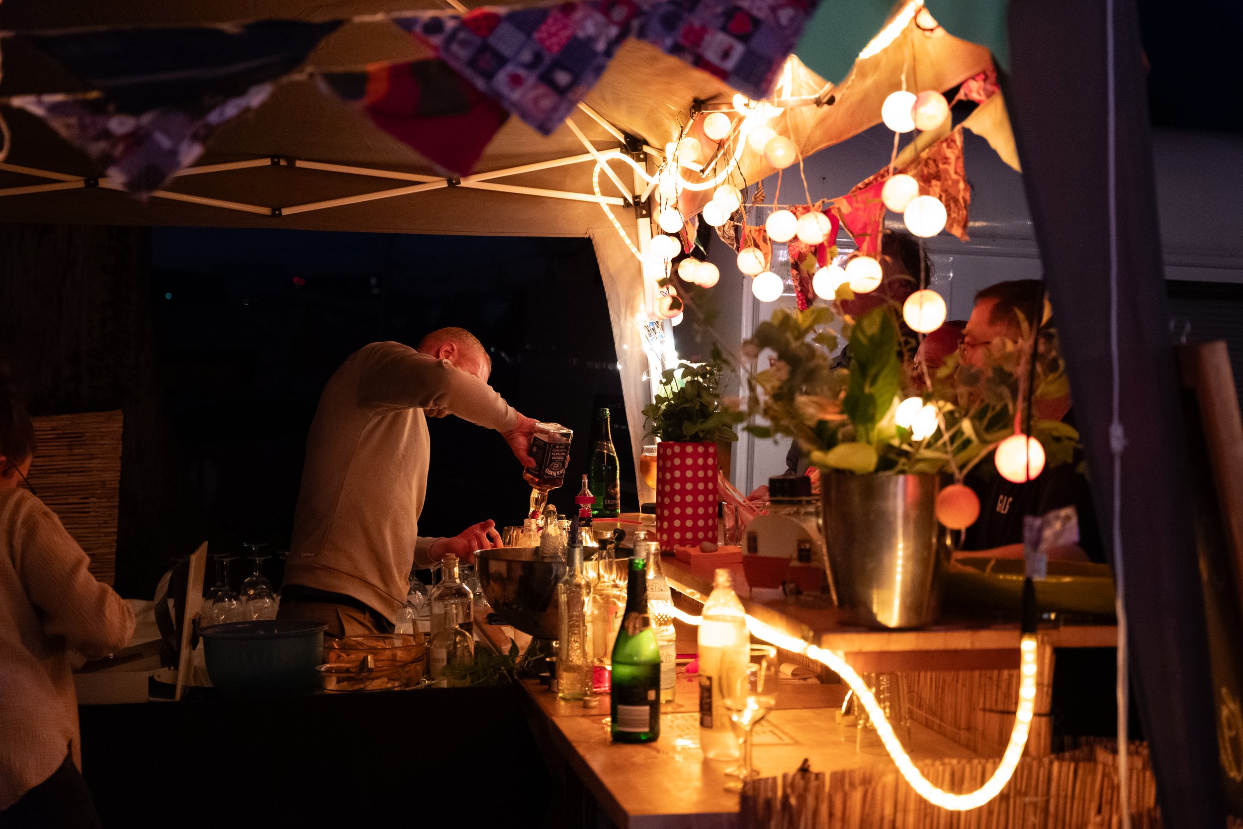 Menschen beim Aufbau eines stimmungsvollen Nachtbars mit Lichterketten, Garnele und Getränke auf dem Tresen, Blumen und Dekorationen im Hintergrund.