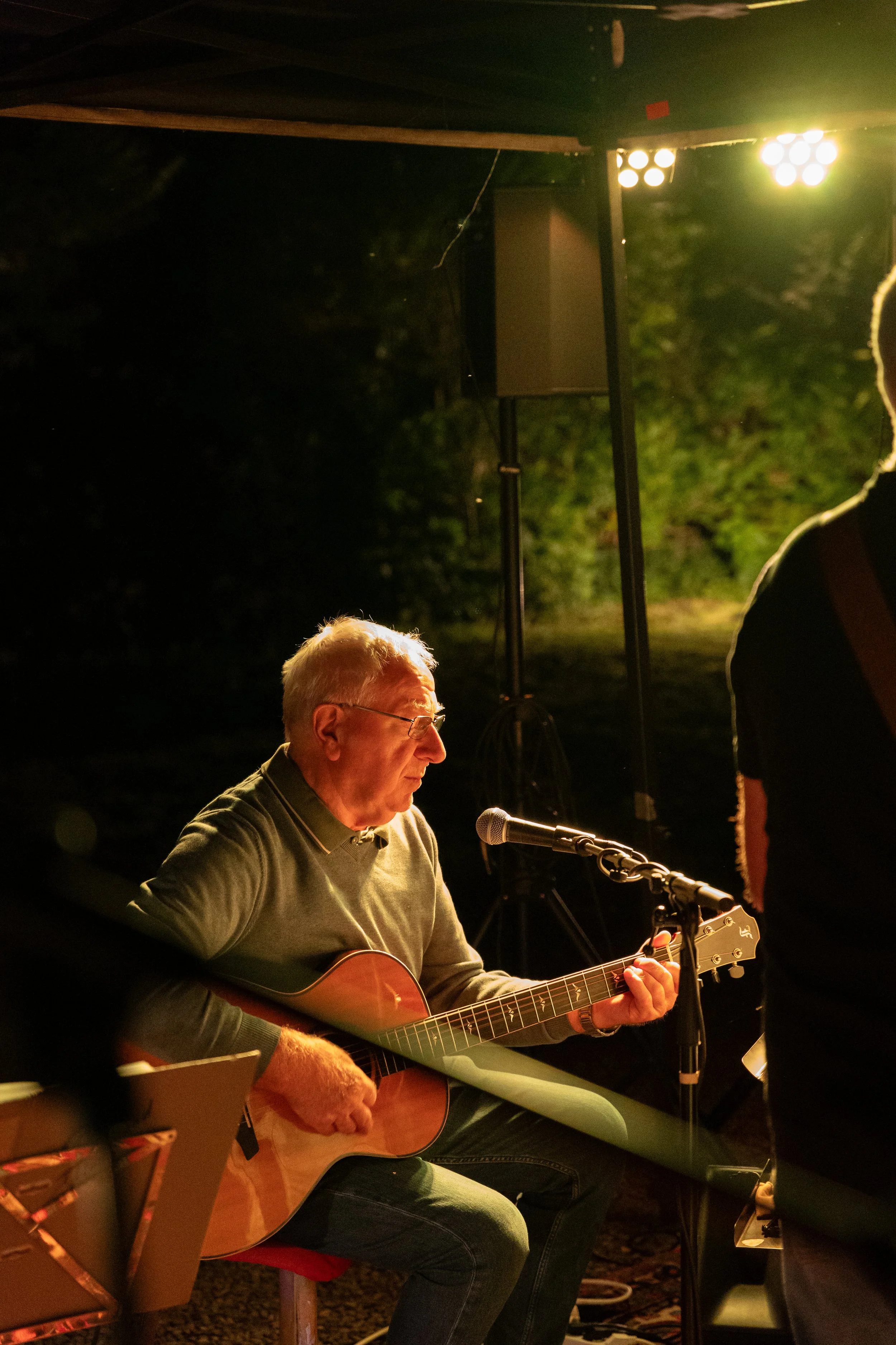 Älterer Mann spielt Gitarre bei einem Open-Air-Konzert, nachts, unter einer Lichtkuppel, schwerer Klang.