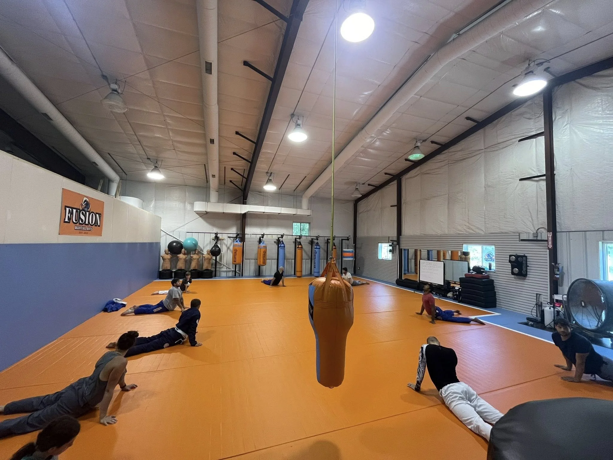 People exercising in a martial arts gym with an orange floor, punching bags, and fitness equipment.