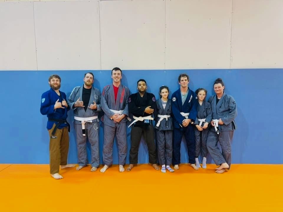 Group of Brazilian Jiu-Jitsu practitioners in gis posing for a photo on a mat.