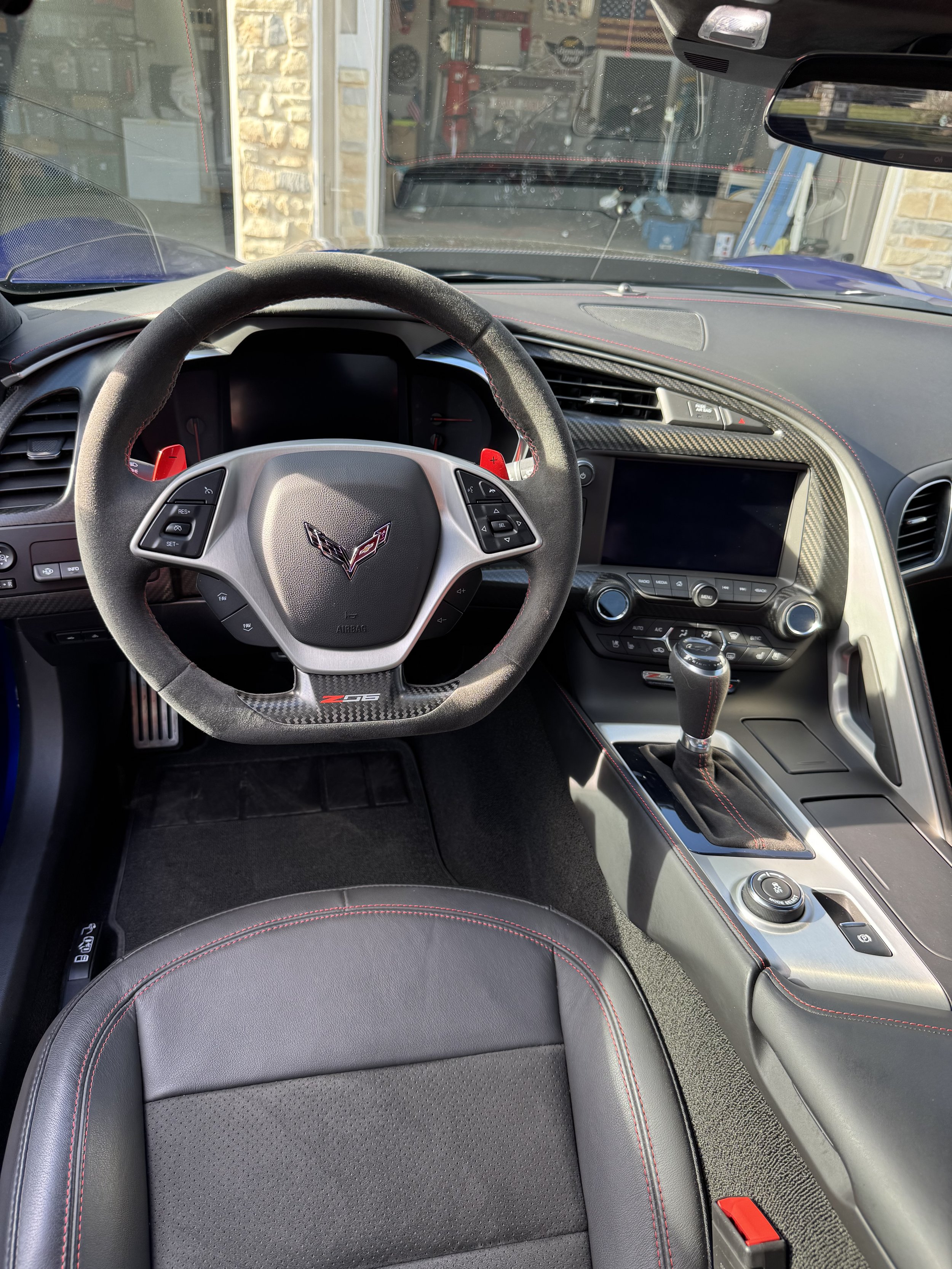 Interior of a Chevrolet Corvette Z06, featuring a leather-wrapped steering wheel with Corvette logo, a central touchscreen, gear shift, and black leather seats with red stitching.