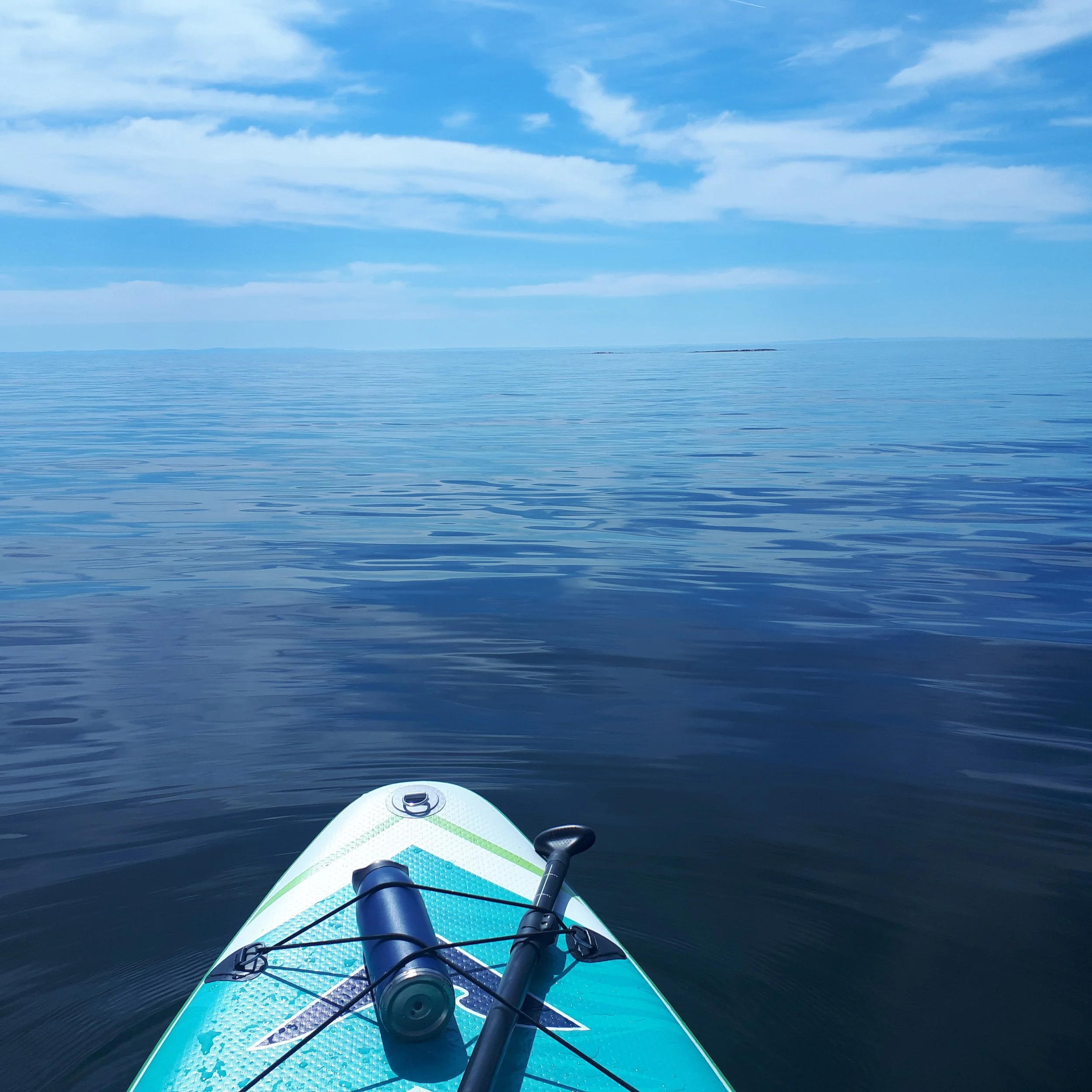 Une planche de paddlebord sur une mer calme avec un ciel bleu et quelques nuages.