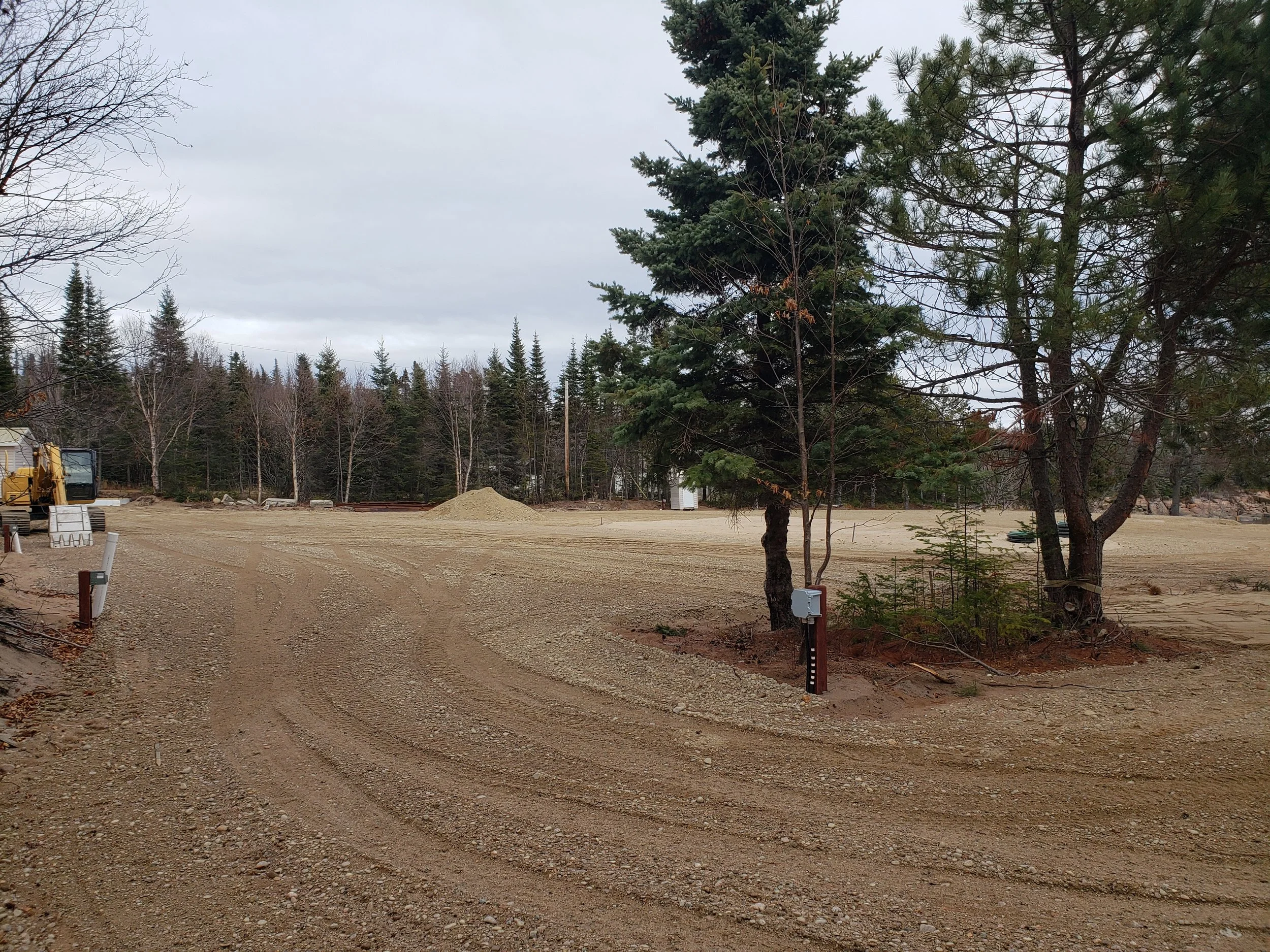 Terrain de chantier avec un camion de construction à gauche, des arbres autour et un ciel nuageux