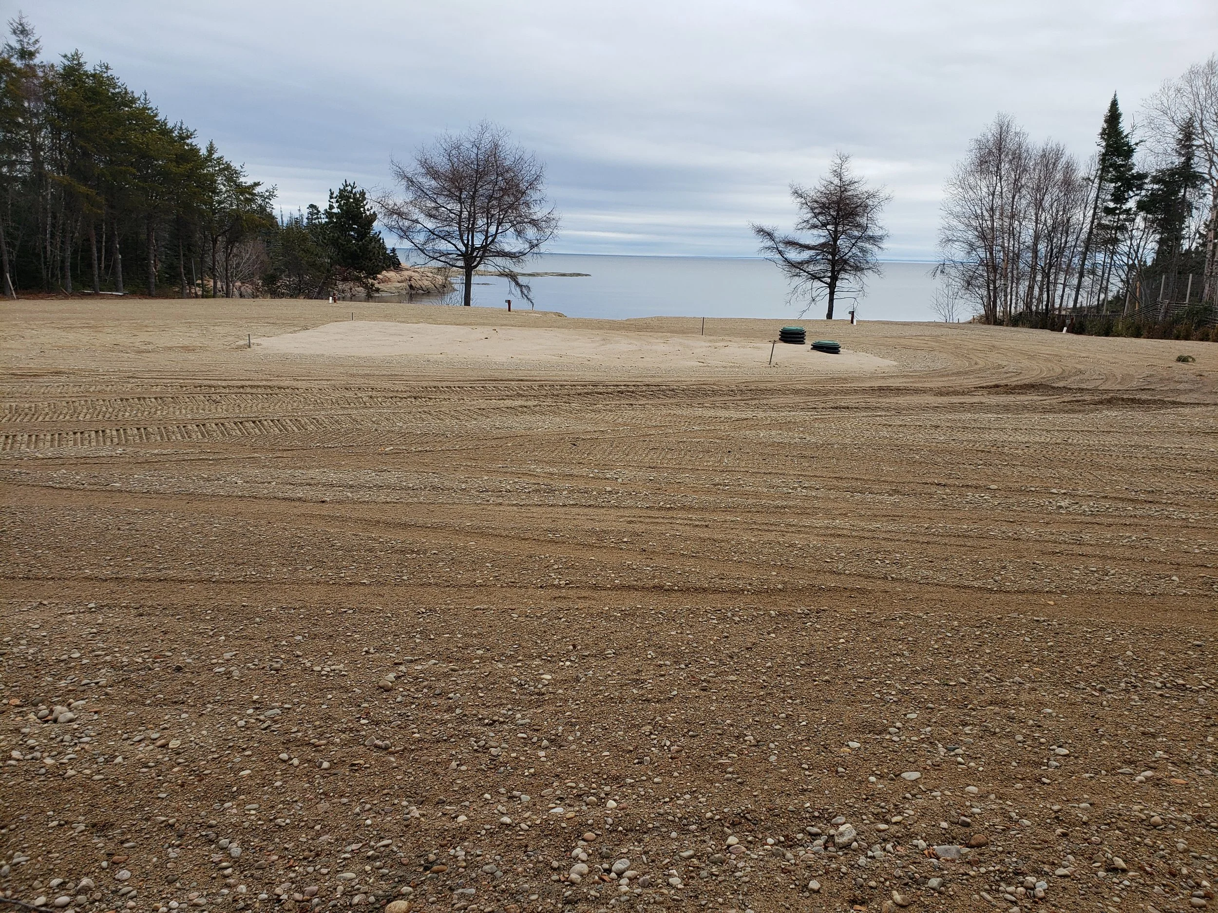 plage en cours de rénovation avec du sable, quelques arbres sans feuilles et le lac en arrière-plan