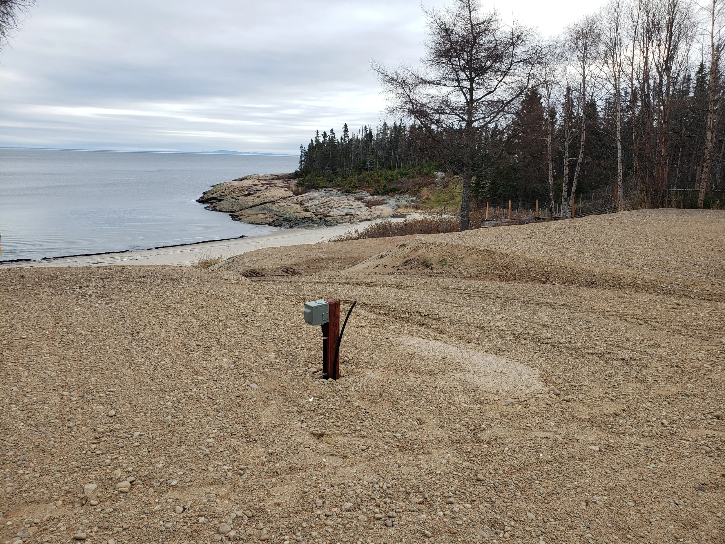Plage rocheuse avec arbres et rochers en arrière-plan sous ciel nuageux.
