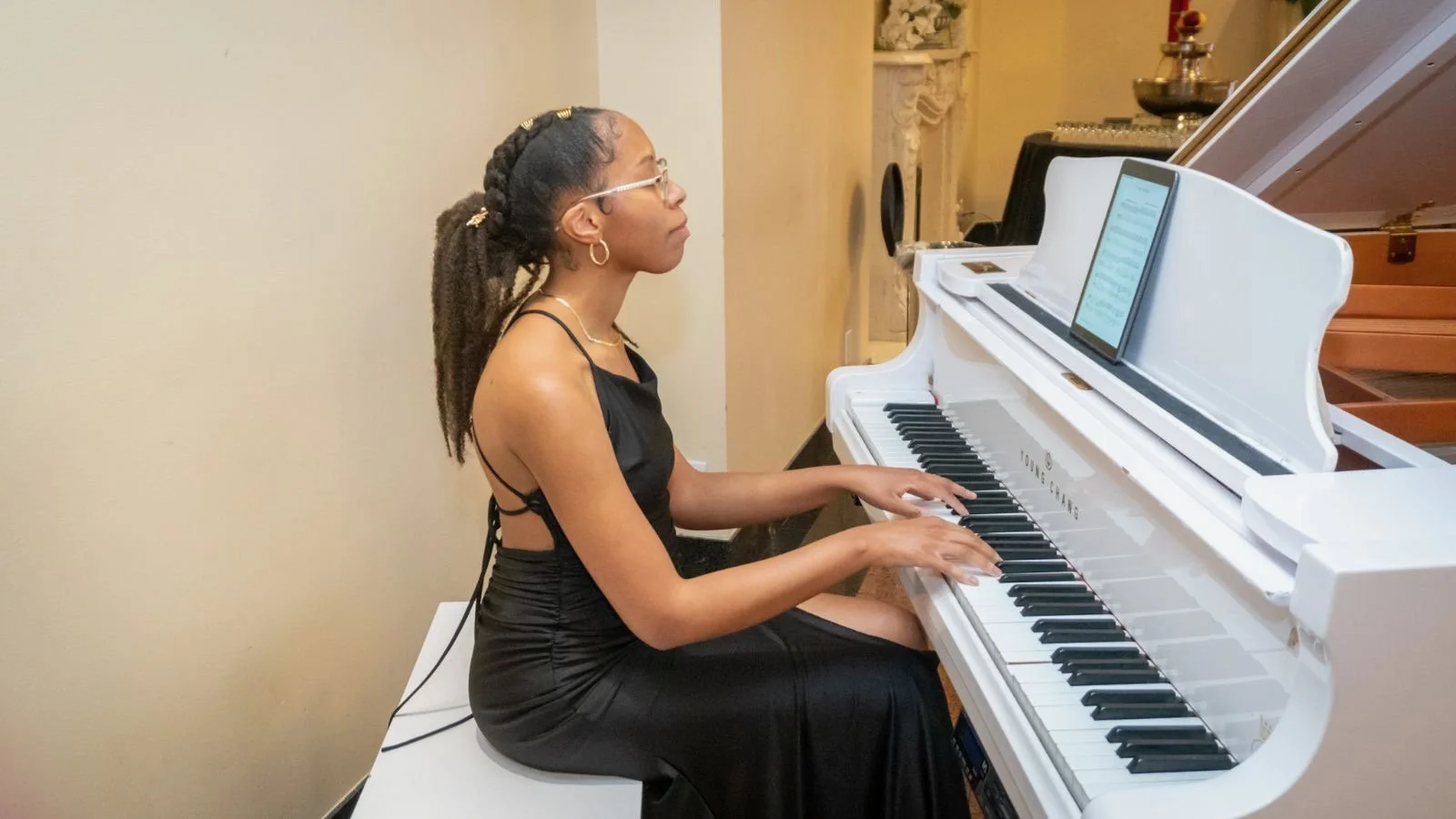 A person in a black dress playing a white grand piano indoors.