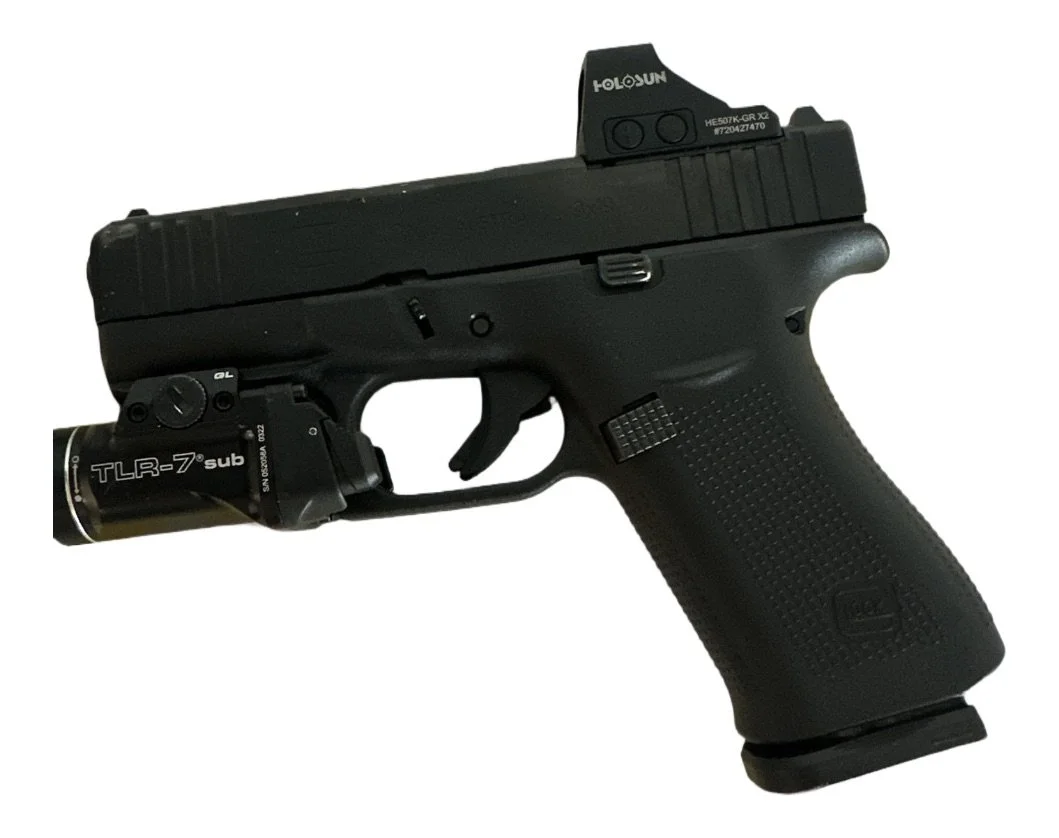 A black semi-automatic handgun with a holographic sight mounted on top and a laser aiming device attached underneath the barrel.