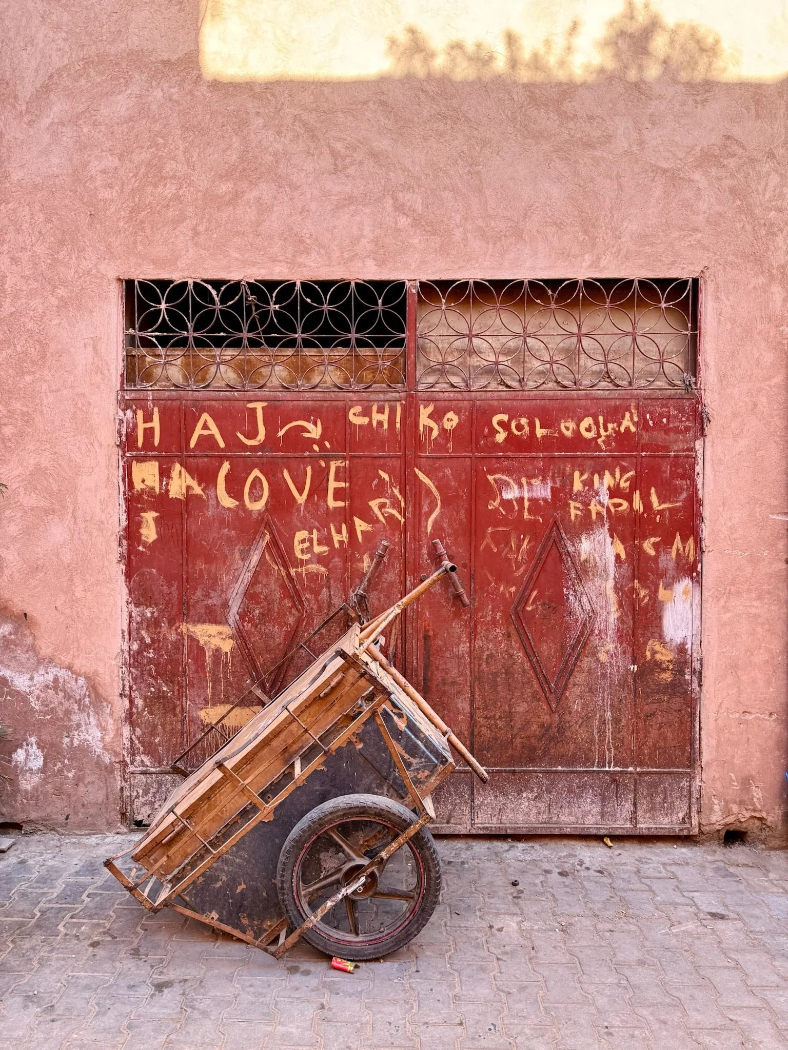 Een rode metalen poort met graffiti, een handkar met houten laden staat voor de poort.