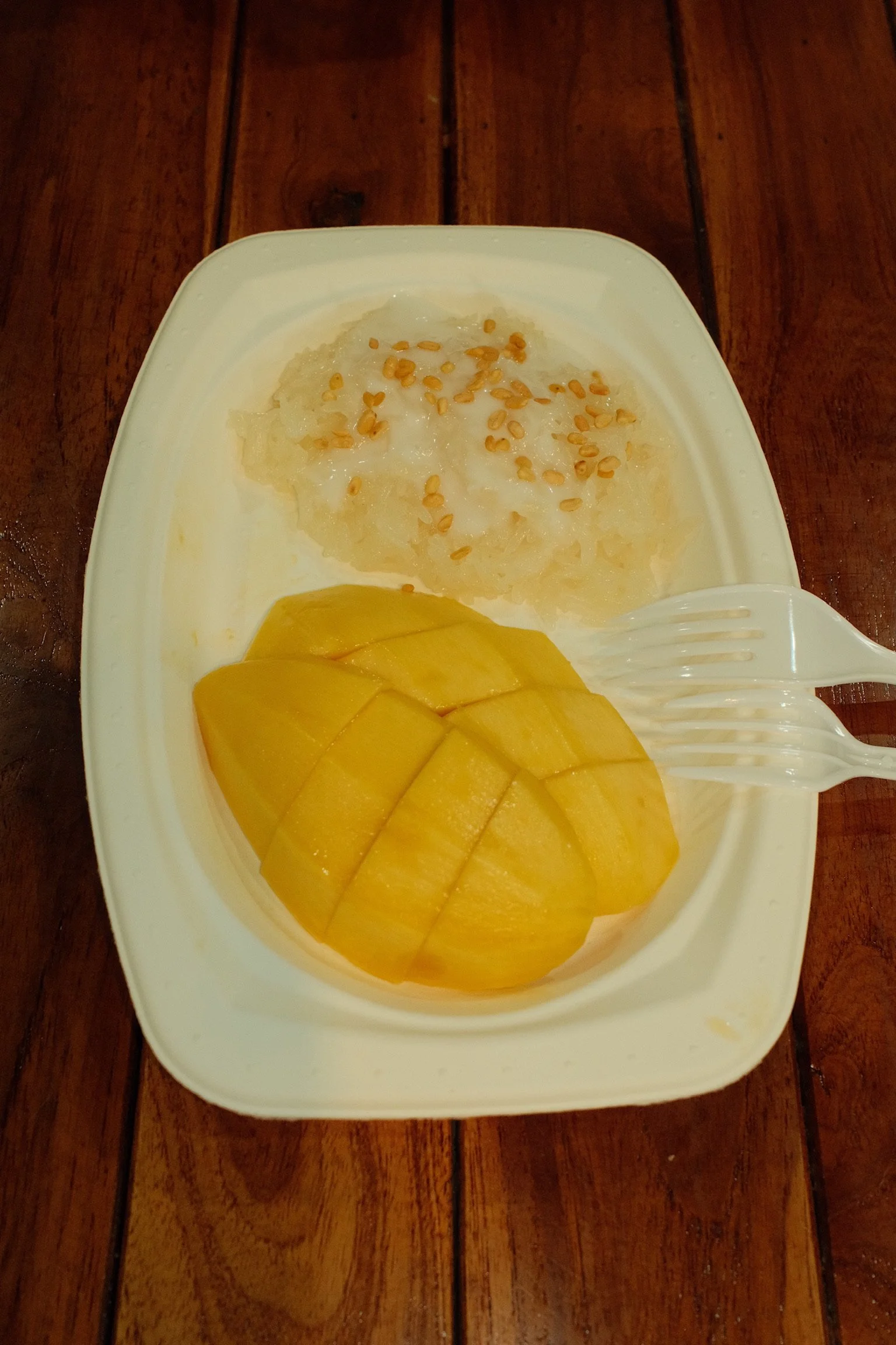 Mango sticky rice op een papieren bordje met zaadjes er naast om te garneren.