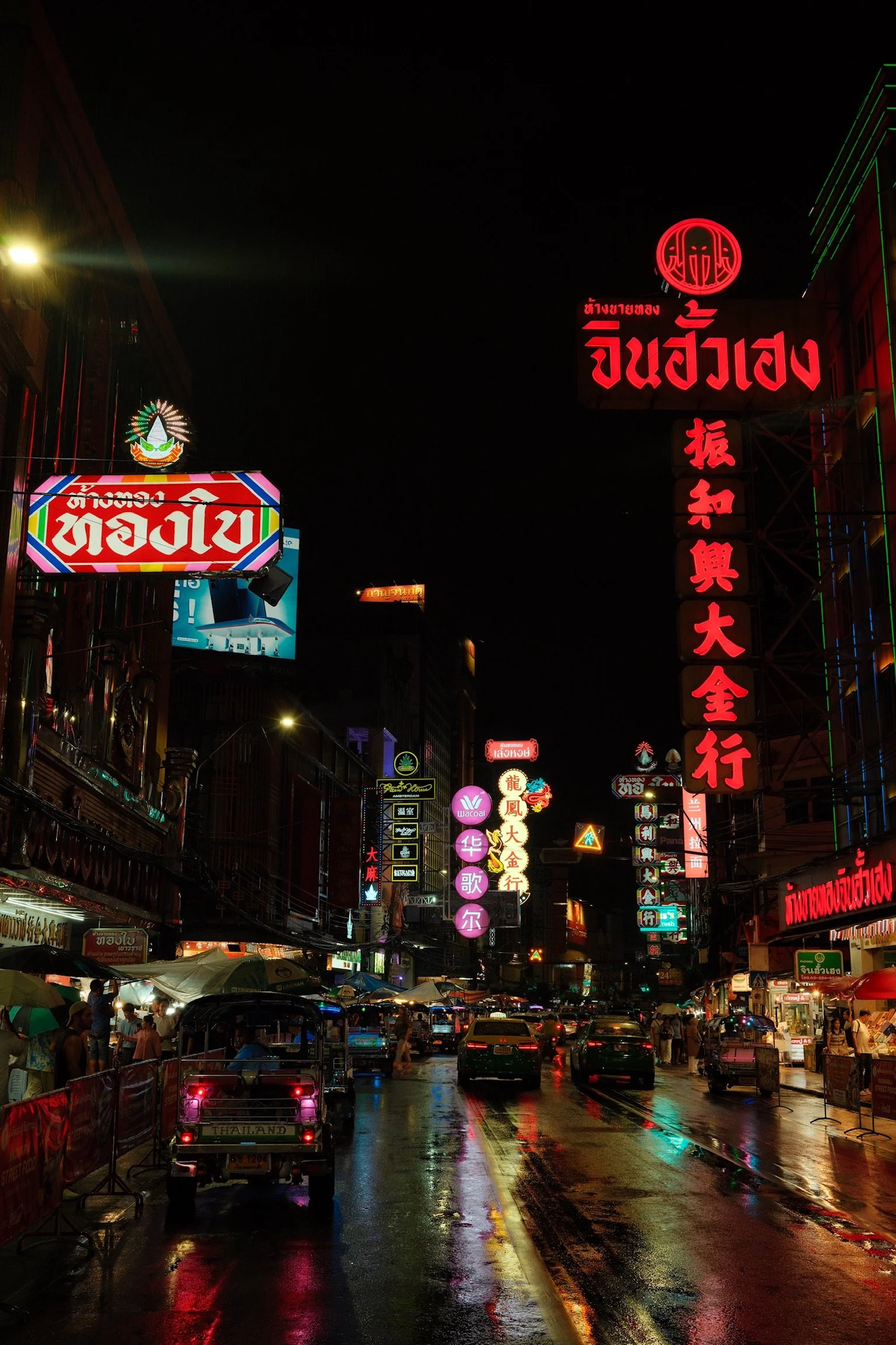 Een drukke straat in Chinatown met neonverlichting en winkels, 's nachts, natte weg met reflekties.
