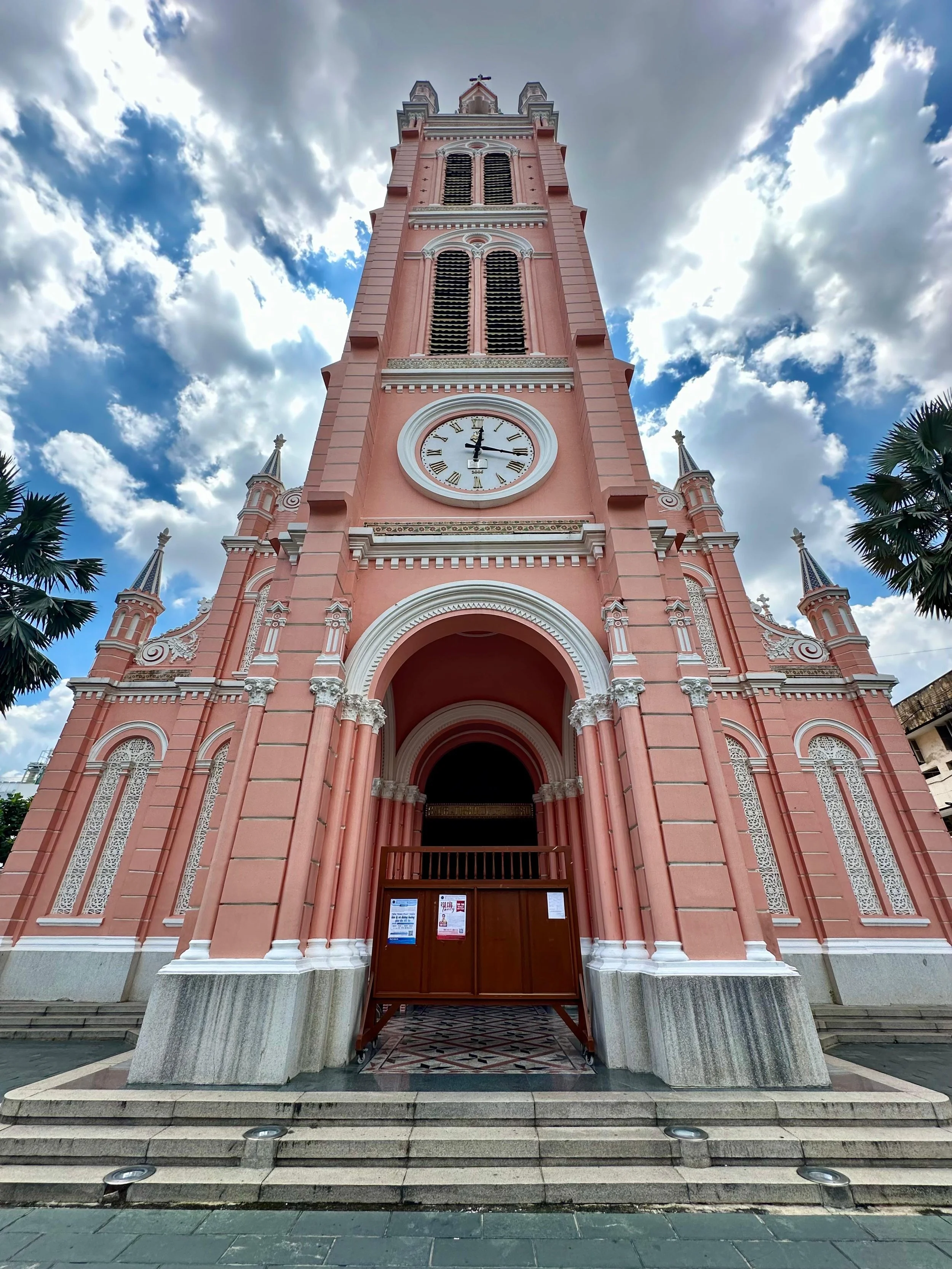 Een roze kerk met een grote toren en een klok, onder een bewolkte hemel.