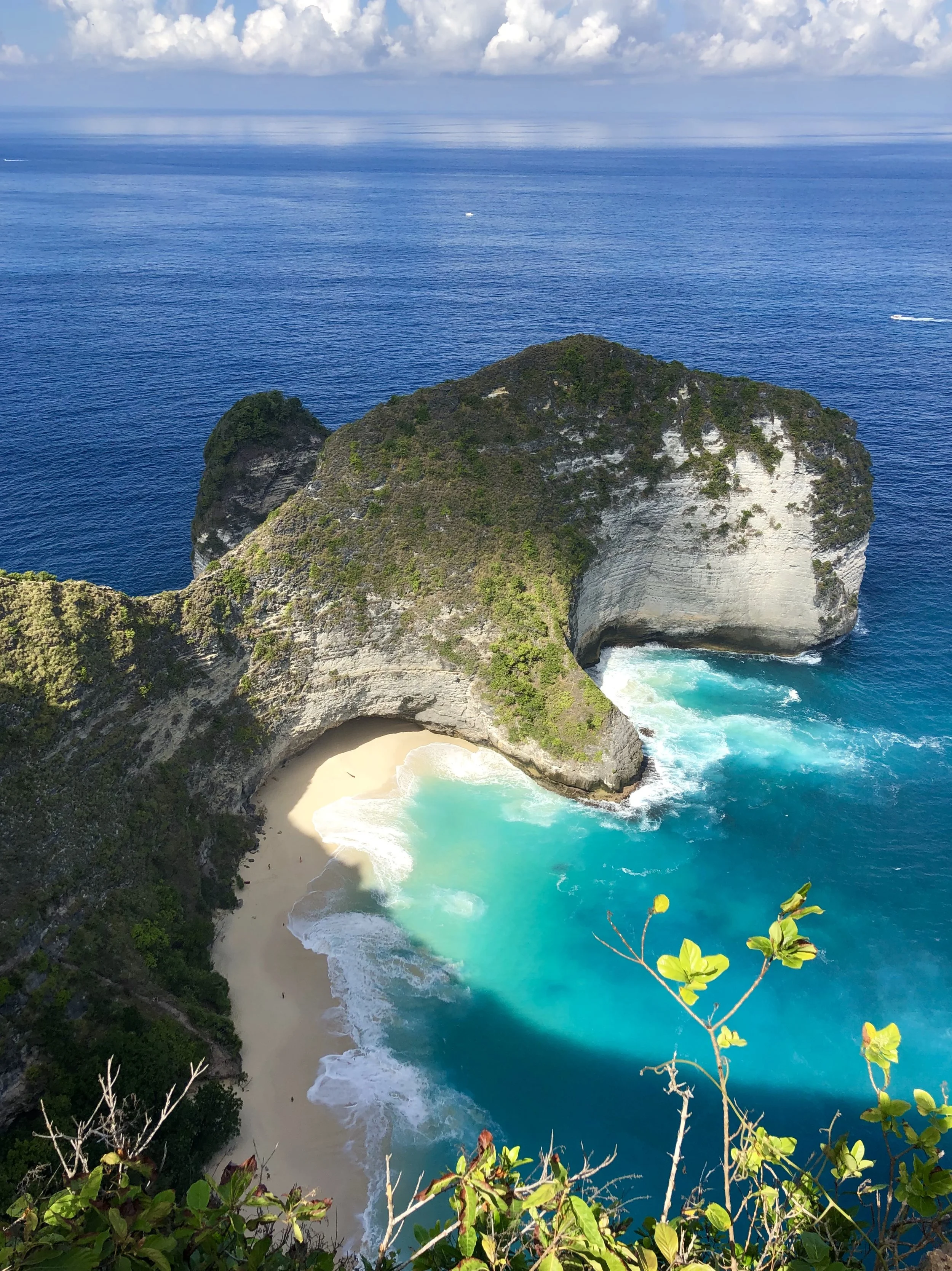 Een kustlijn met een grot en een strand, omgeven door groene heuvels en blauwe oceaan, met een ondergaande zon en een heldere lucht.