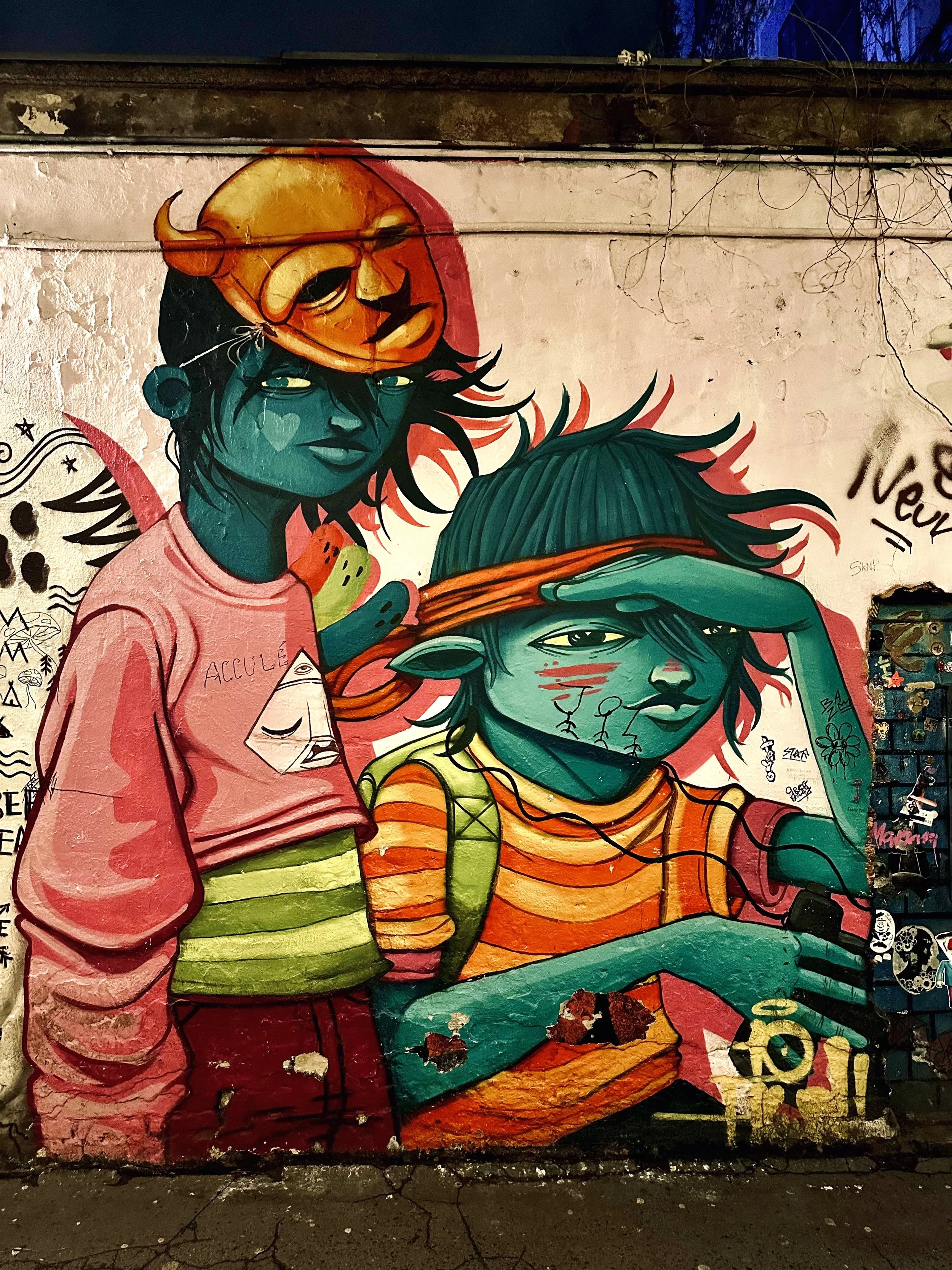 Graffiti van twee jonge mensen met gemengde huidtinten, een met een masker op en een met een hoofdband, tegen een muur met andere tekeningen en teksten.