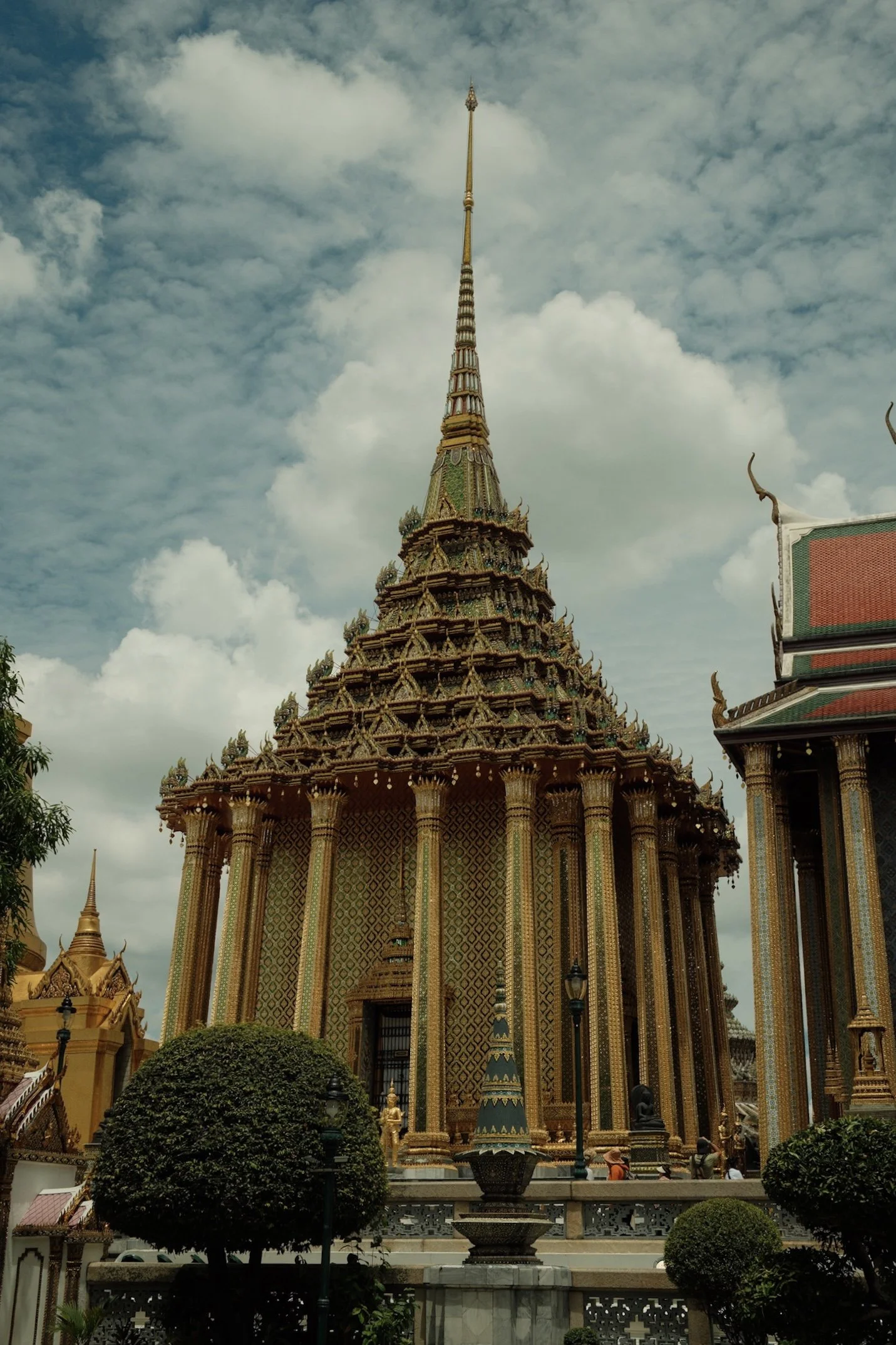 Een traditionele, gedetailleerde tempel met een hoge, spits toelopende torenspits, versierd met gouden en groene decoraties, onder een bewolkte sky.