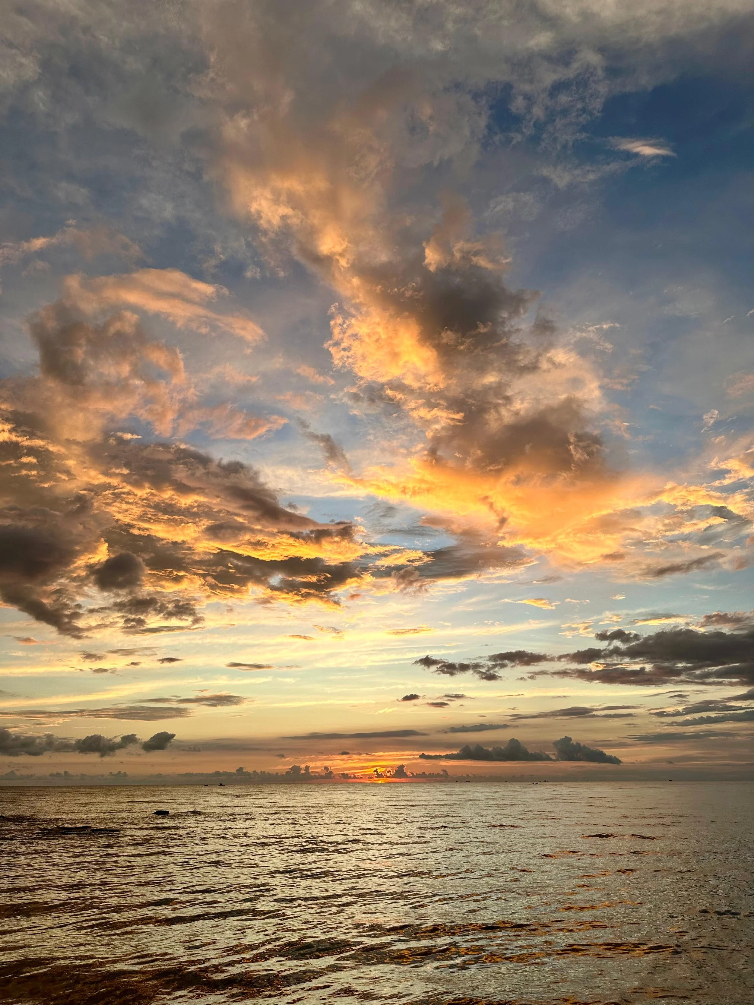 Een zonsondergang boven de oceaan met een kleurrijke hemel vol oranje en blauwe tinten en enkele wolken.