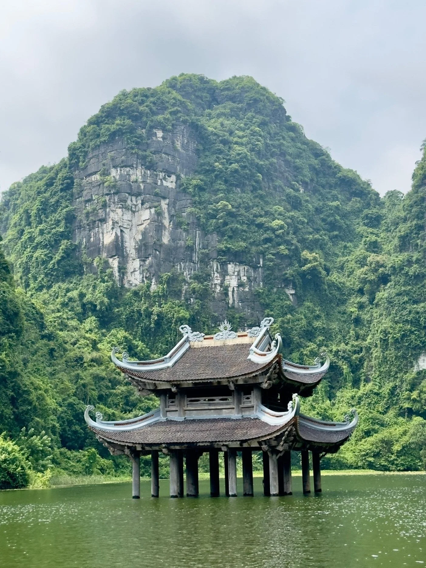 Traditioneel Aziatisch paviljoen op het water met groene bergen op de achtergrond.