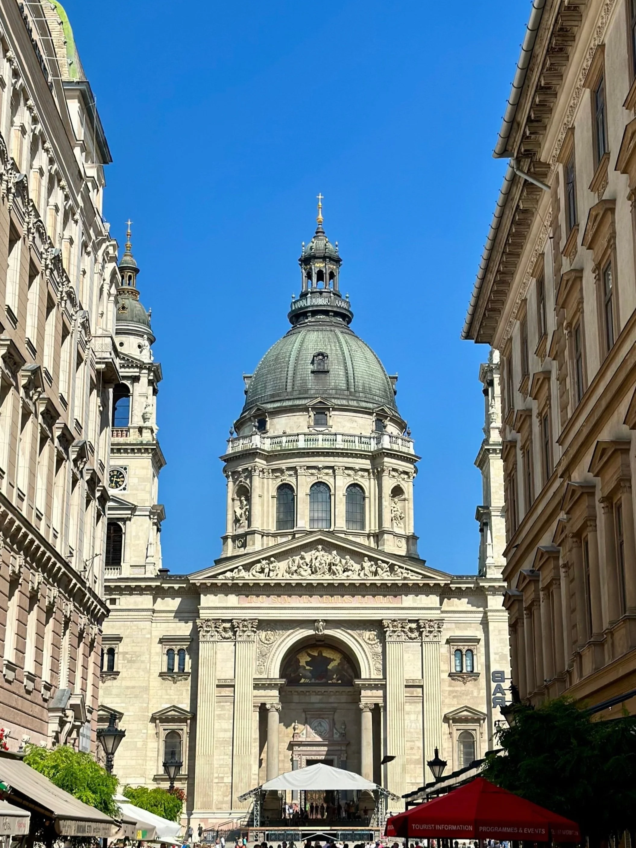 Een grote historische kathedraal met een koepel en een klokkentoren, geflankeerd door bijbehorende gebouwen. Voor de kathedraal staan toiletten en een parasol met toeristeninformatie.