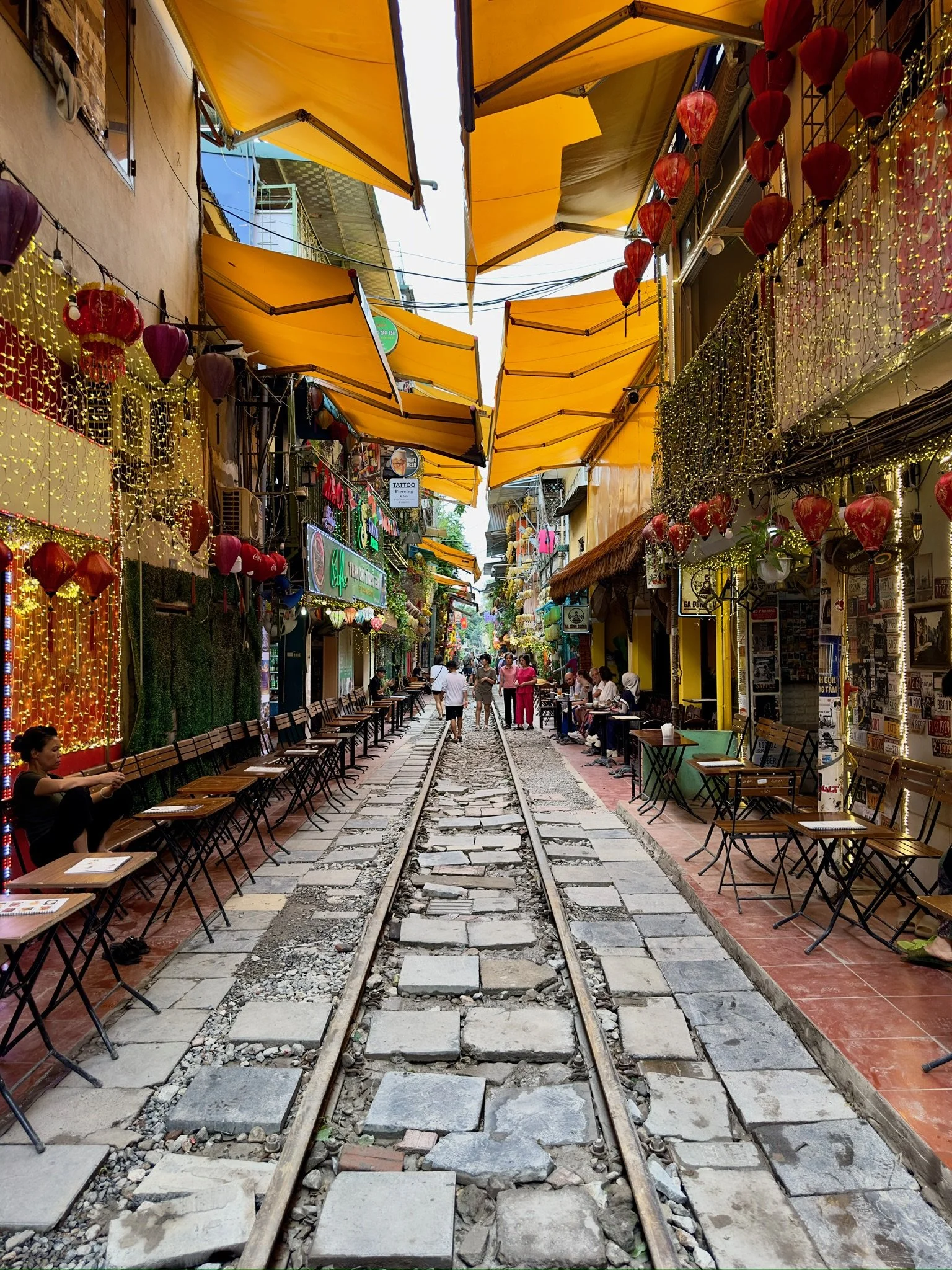 Kleine straat met zitplaatsen langs de rails, kleurrijke lantaarns en decoraties, overdekt door gele markiezen.