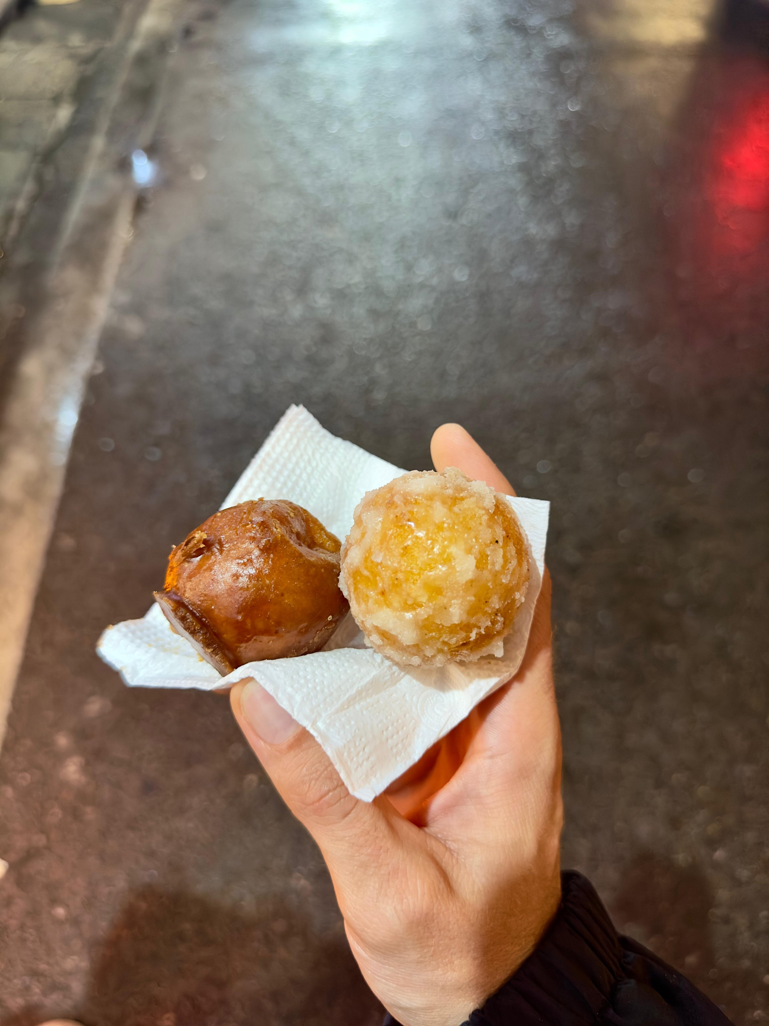 Hand houdt twee verschillende gekleurde en textuurrijke snacks, een in een papieren doekje met een metalen straat en gedoete achtergrond.